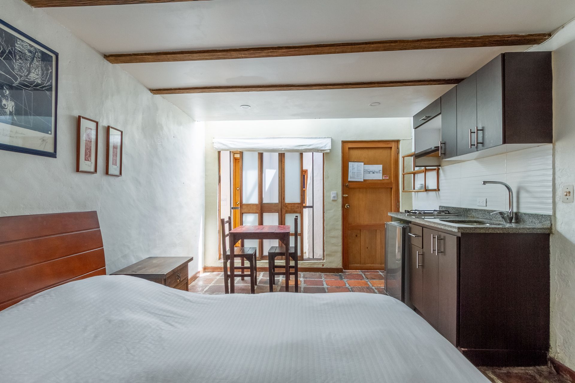 A bedroom with a bed , table and chairs and a kitchen.