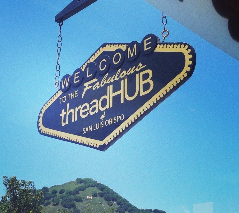 Welcome sign for the fabulous threadHUB, hanging against a blue sky in San Luis Obispo.