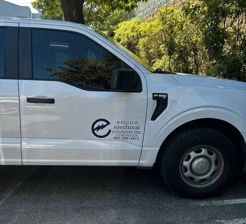 White utility van with company logo parked outdoors beside trees and a hillside.