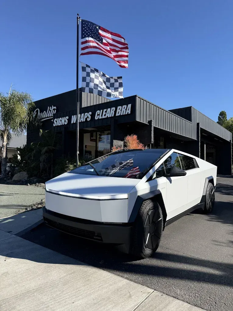 Tesla Cybertruck parked outside a car wash with American and checkered flags flying above.