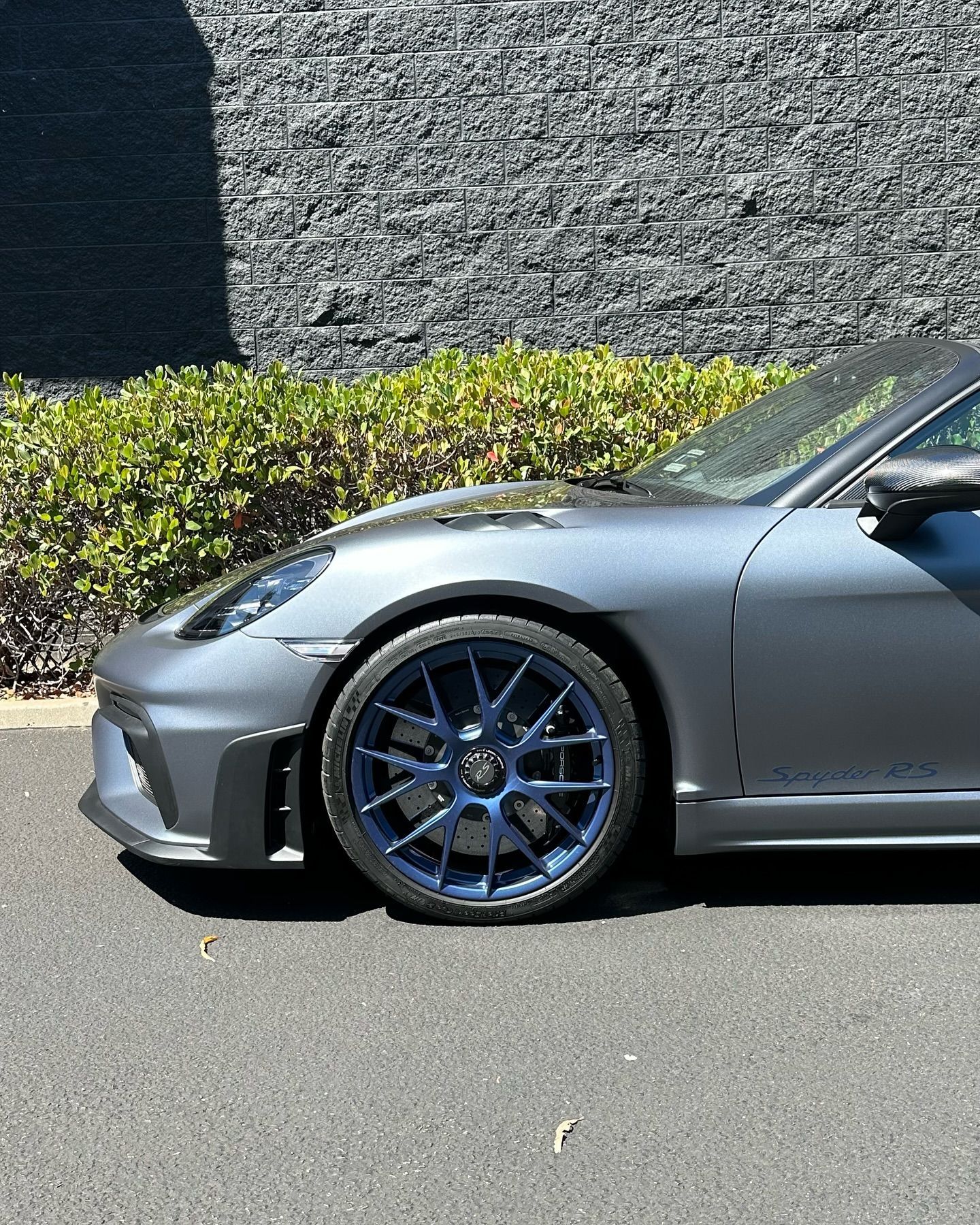 Silver sports car parked outdoors, showing the front wheel and side with blue rims.