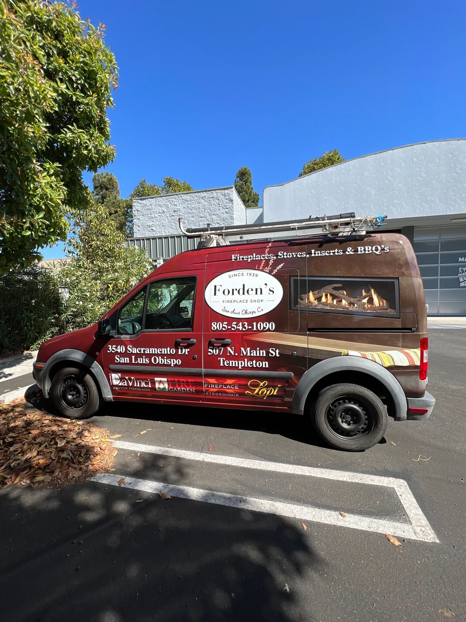 Red food truck parked in a sunny lot with trees and a blue sky nearby