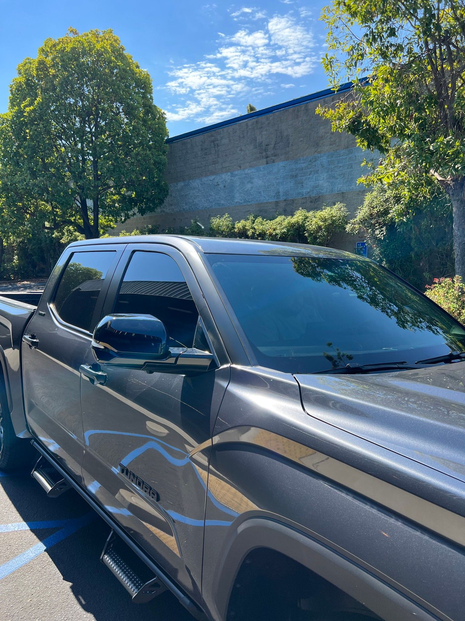 Black pickup truck parked by a brick building under bright blue sky and trees