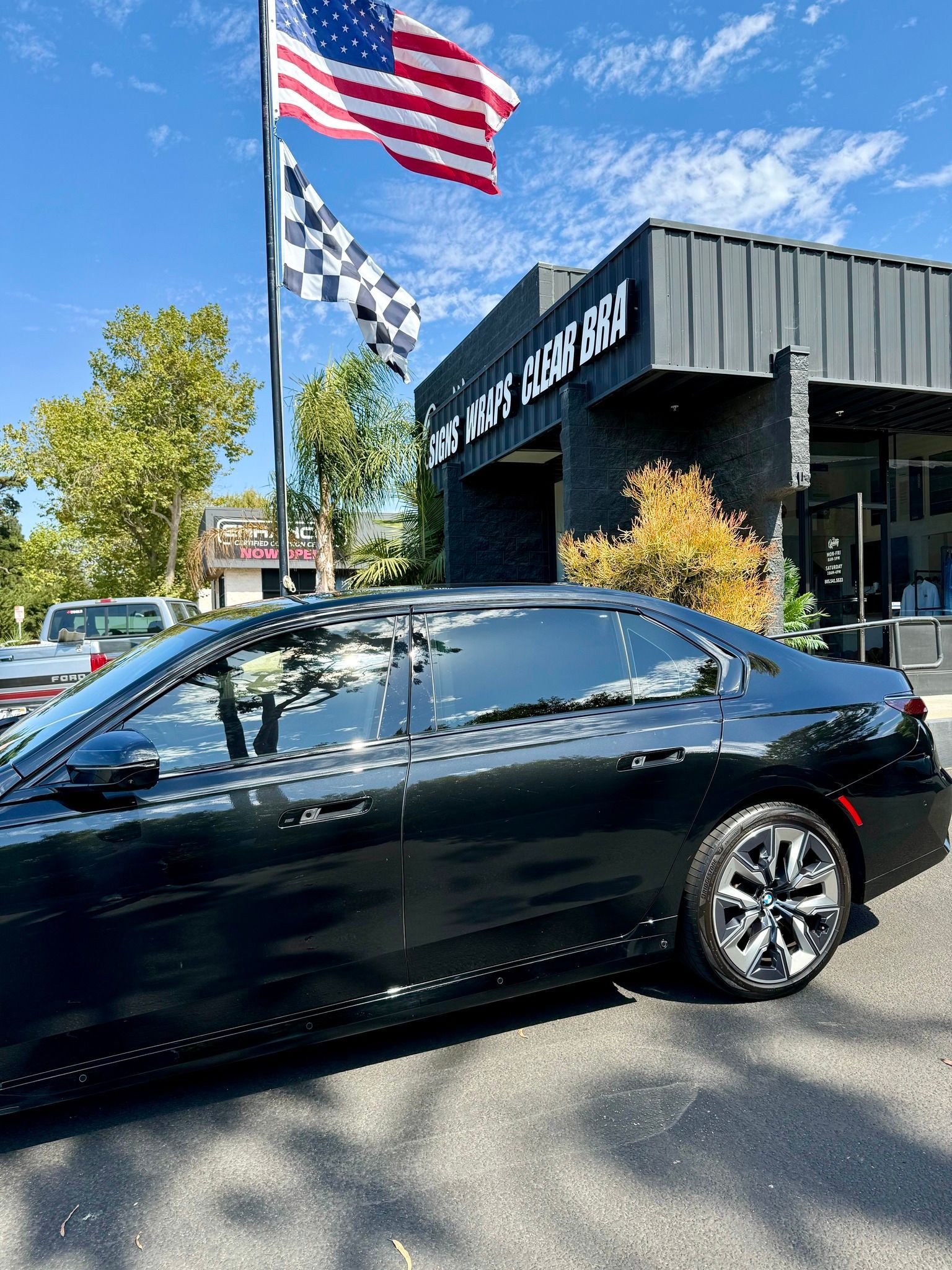 Black sedan parked outside a dealership with American and checkered flags flying above it