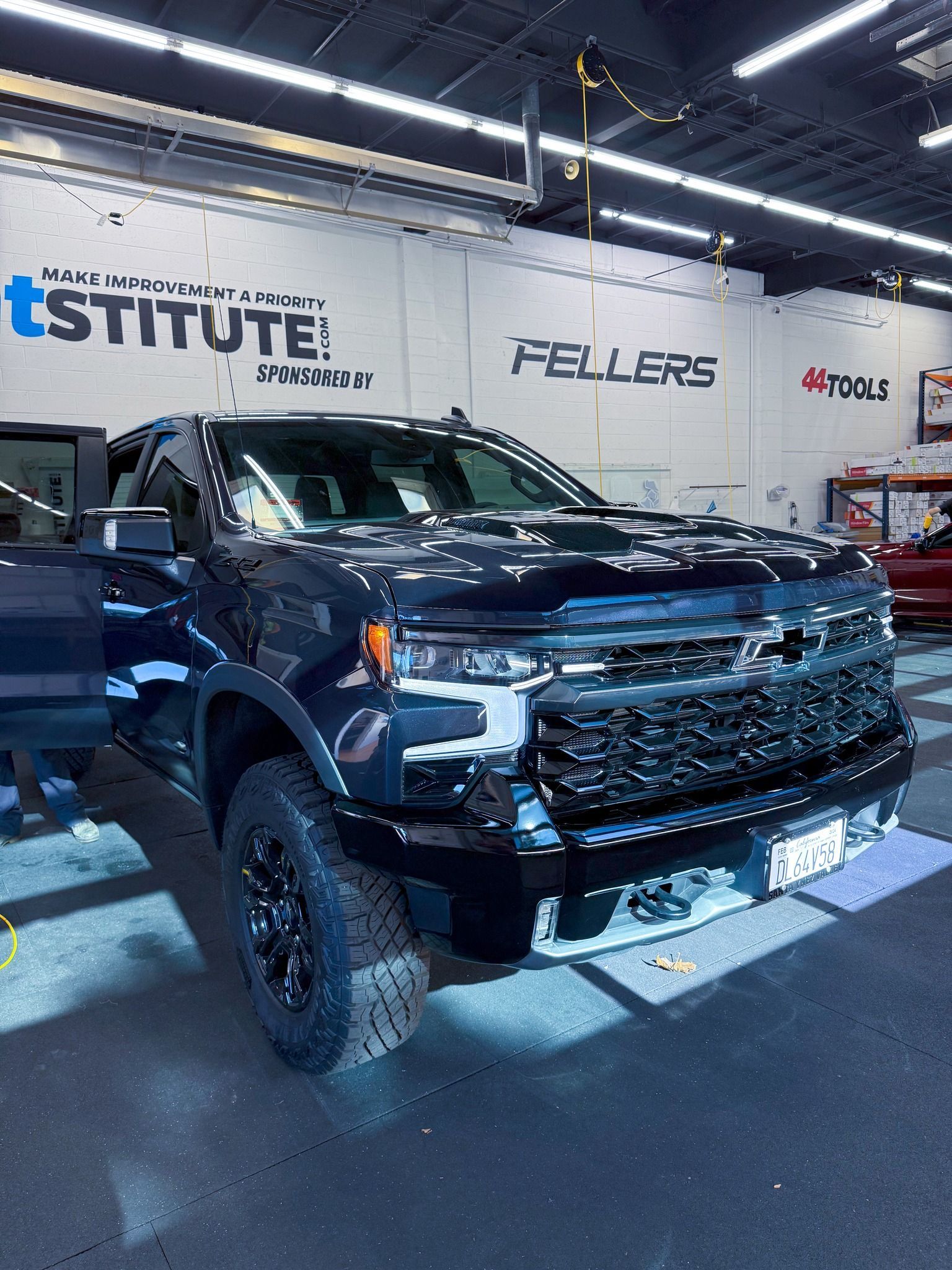 Black lifted pickup truck in an indoor auto shop with bright overhead lights.
