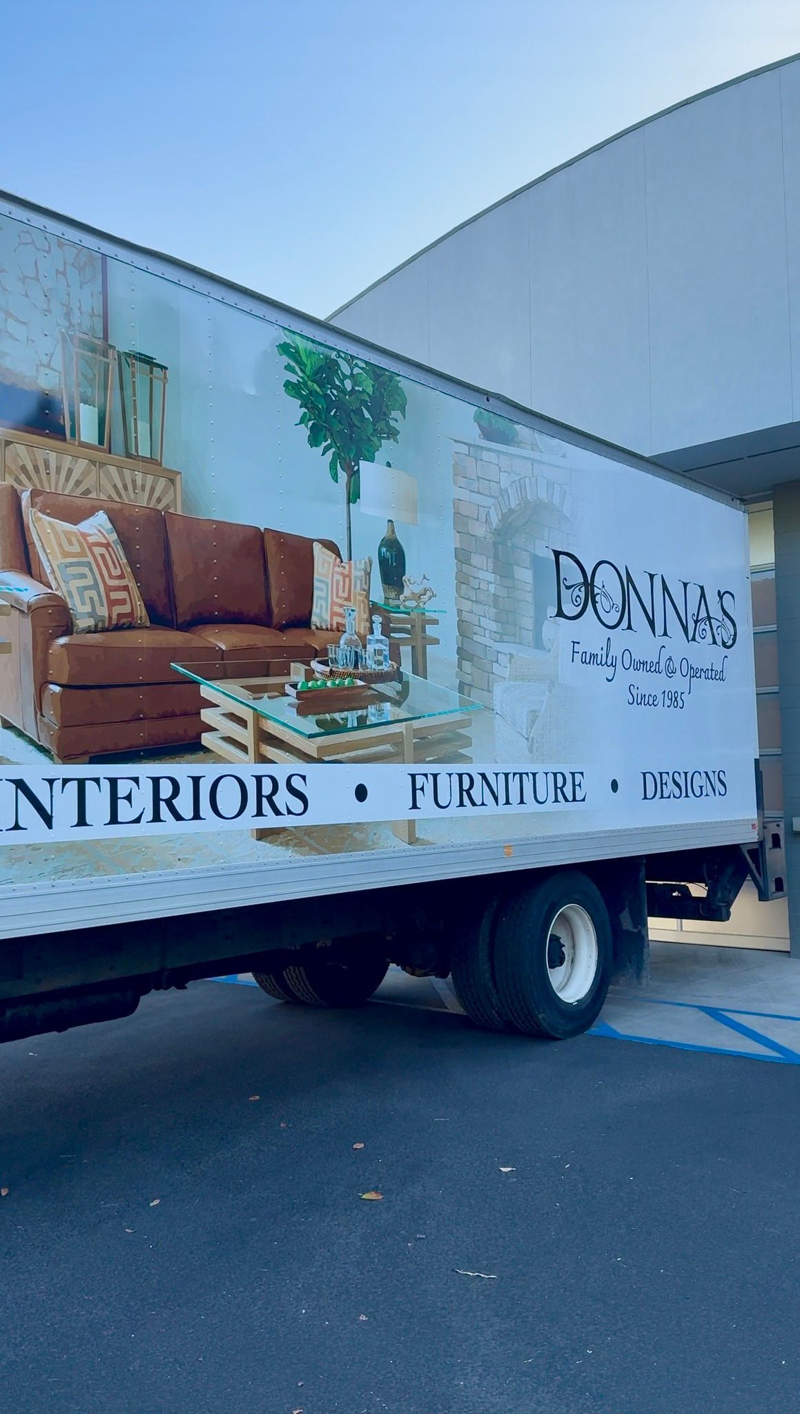 Delivery truck with mural of a brown sofa and “interiors” branding parked outdoors