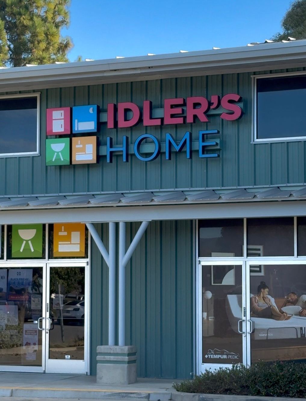 Storefront sign reading “IDLER’S HOME” on a teal building with colorful square icons above the entrance