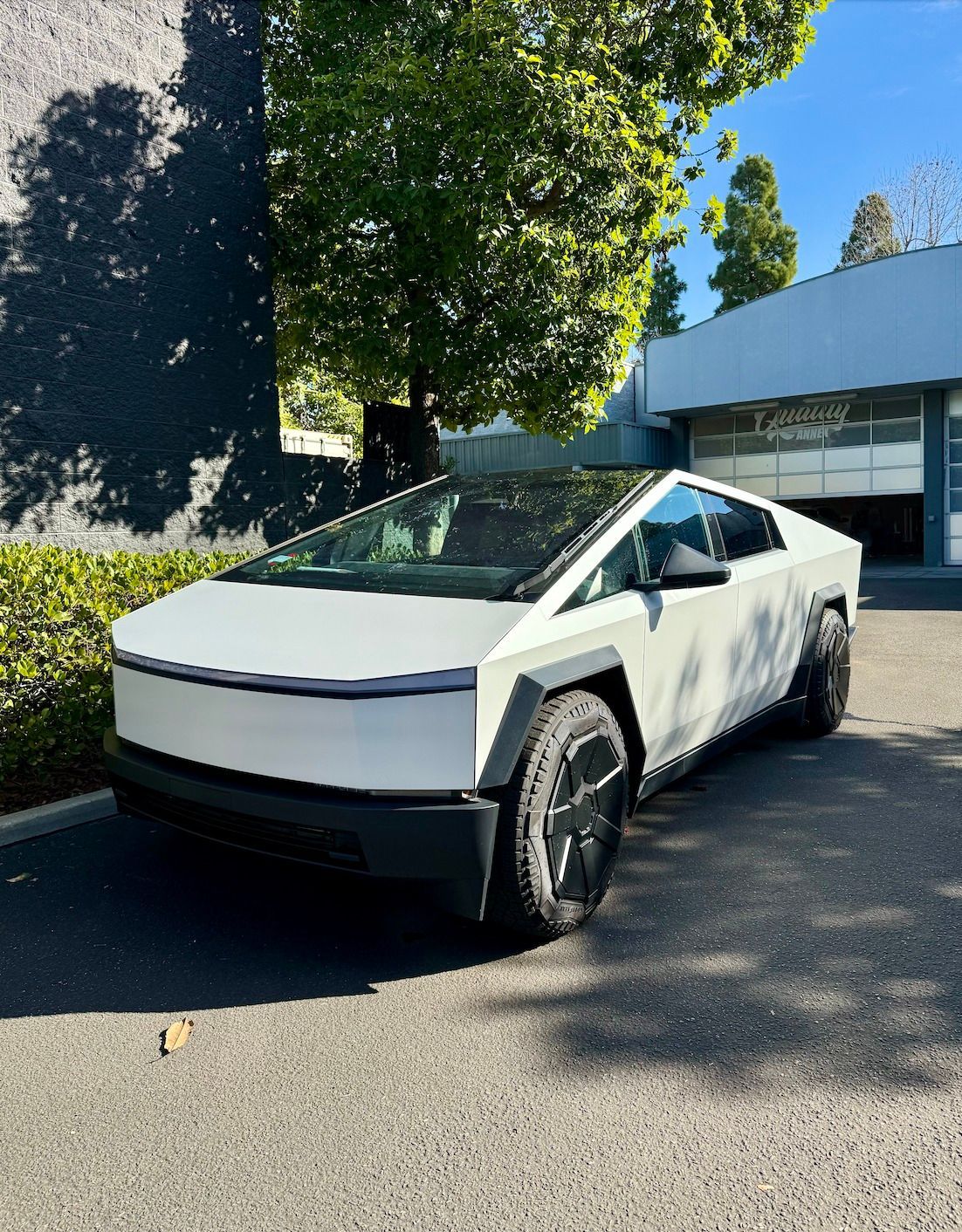White Tesla Cybertruck parked outdoors in sunlight beside a modern building and trees
