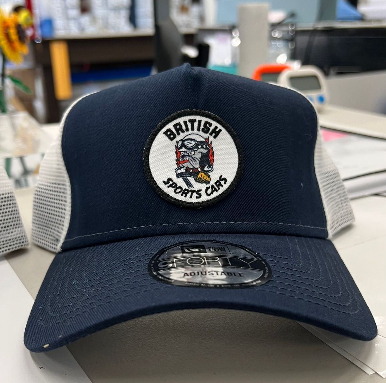 Navy and gray trucker cap with a British Sports Car patch displayed on a table.