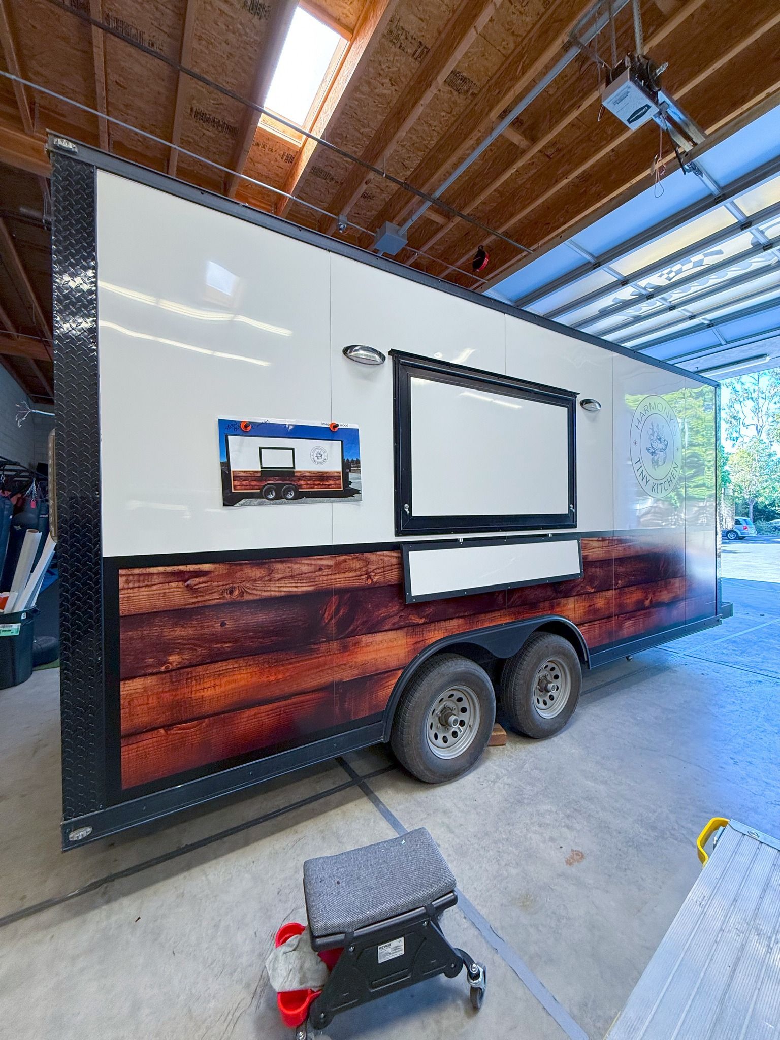 Custom trailer with white side panel, large window and mounted screen inside a covered workshop.