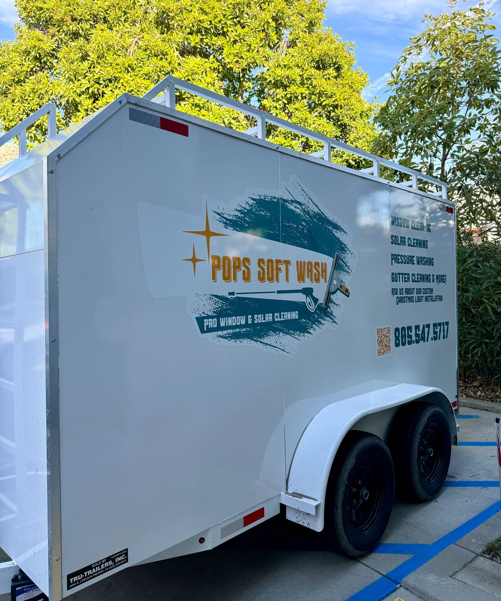 White trailer with gold logo parked in a lot, with trees and blue parking lines in the background