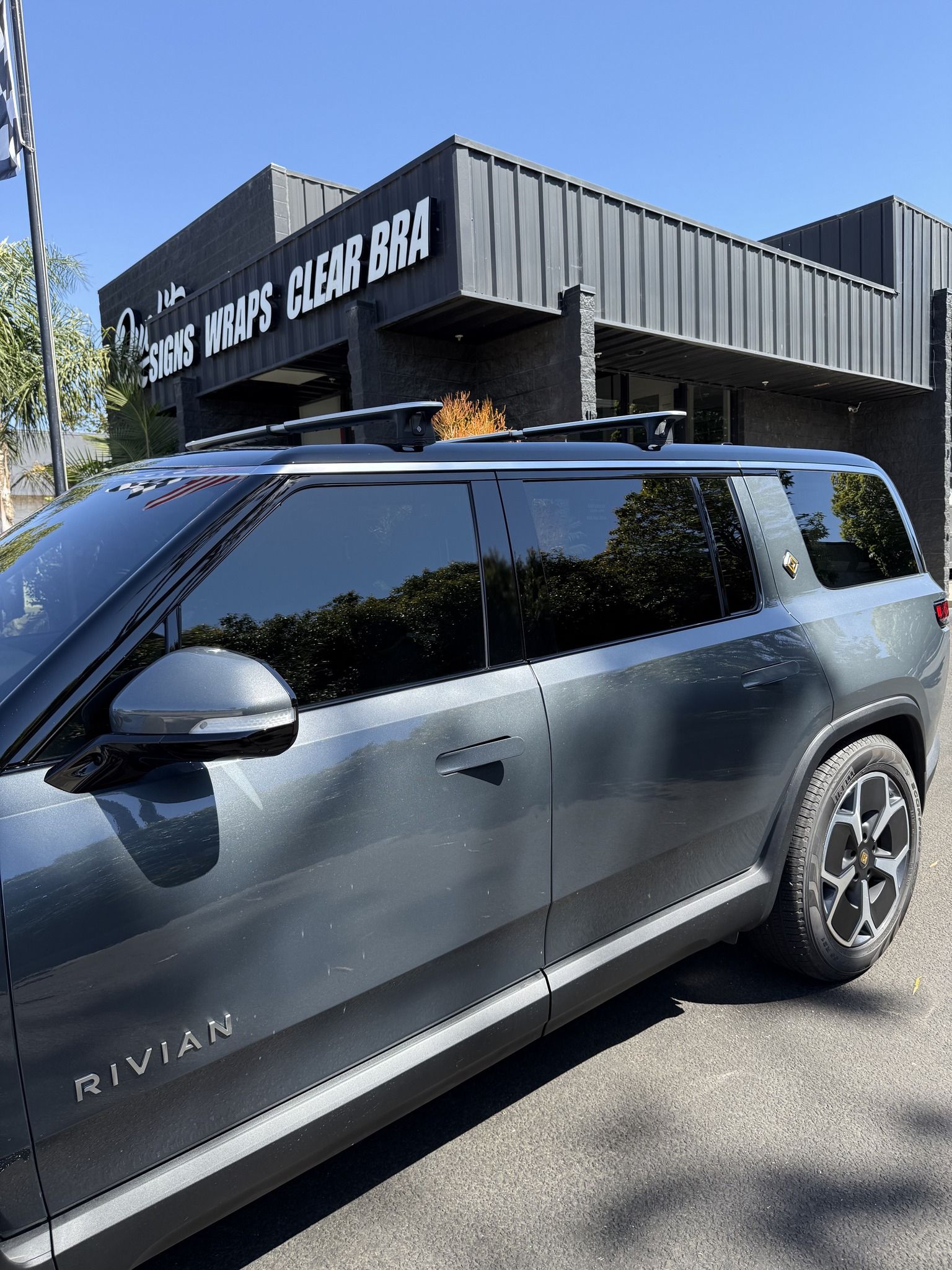Gray Rivian SUV parked outside a black building with a sign reading “The Black Caesar BBQ.”