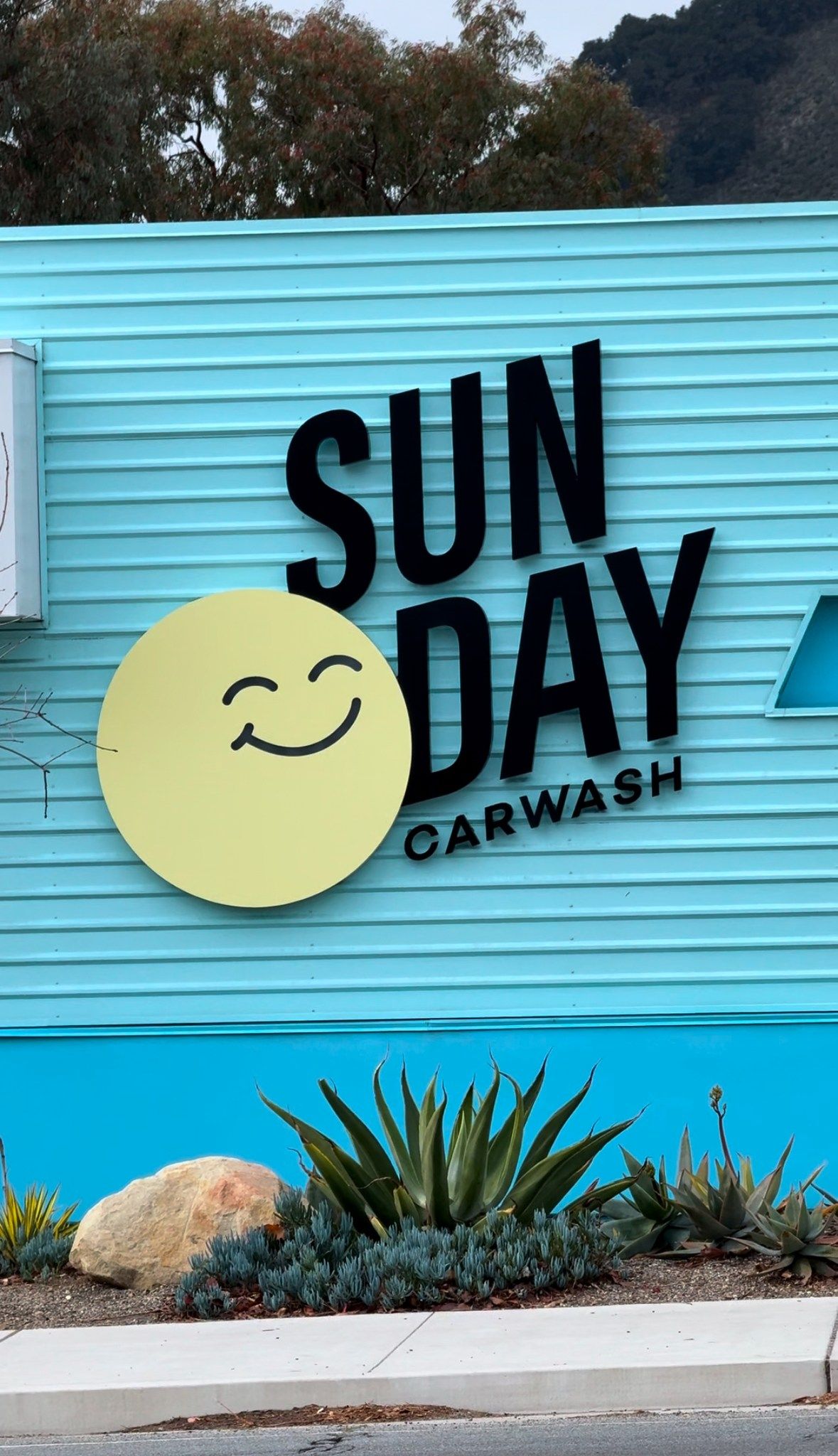 Sun Day Car Wash sign on a blue wall with a smiling yellow sun logo