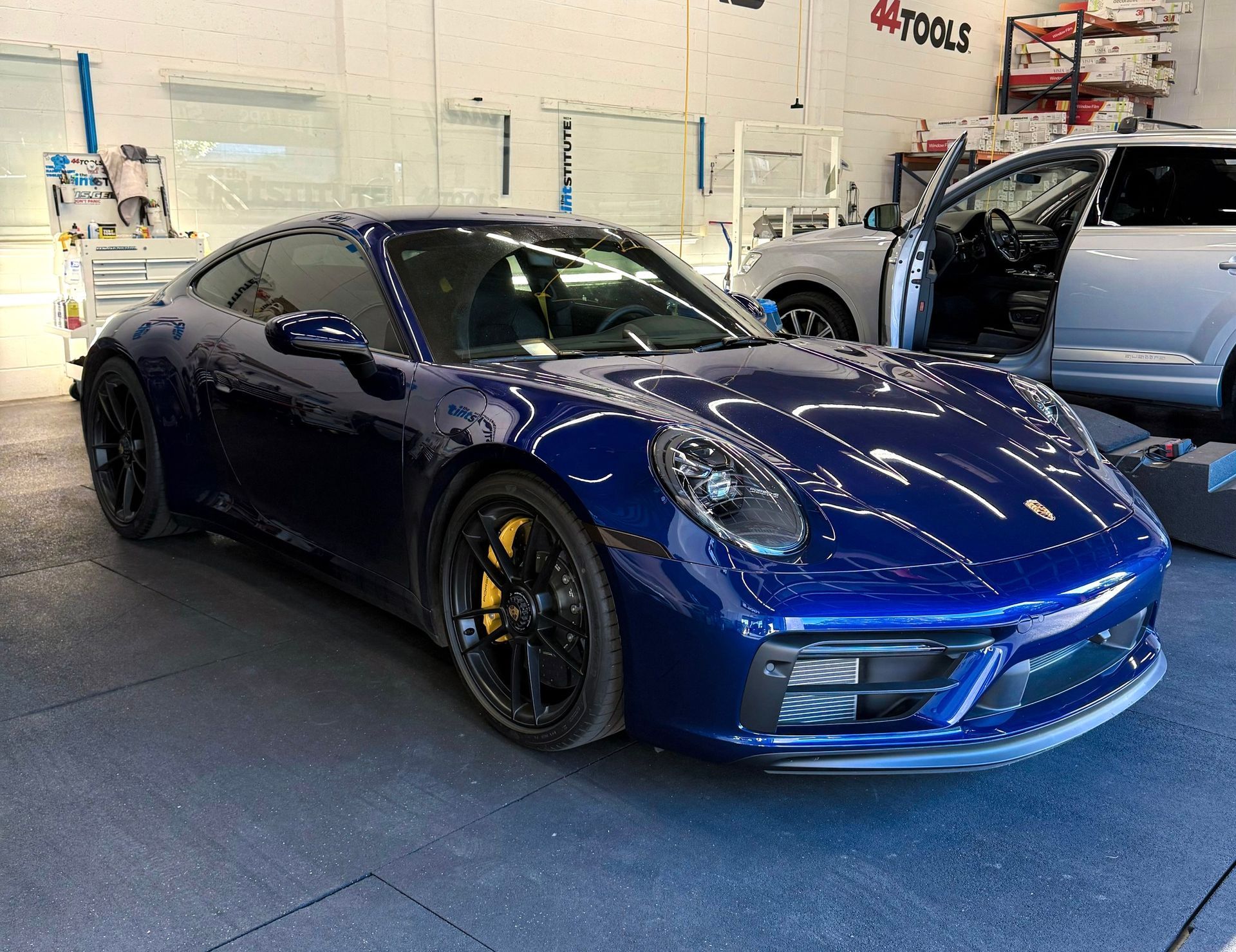 Blue Porsche sports car parked indoors beside an open silver SUV in a garage.