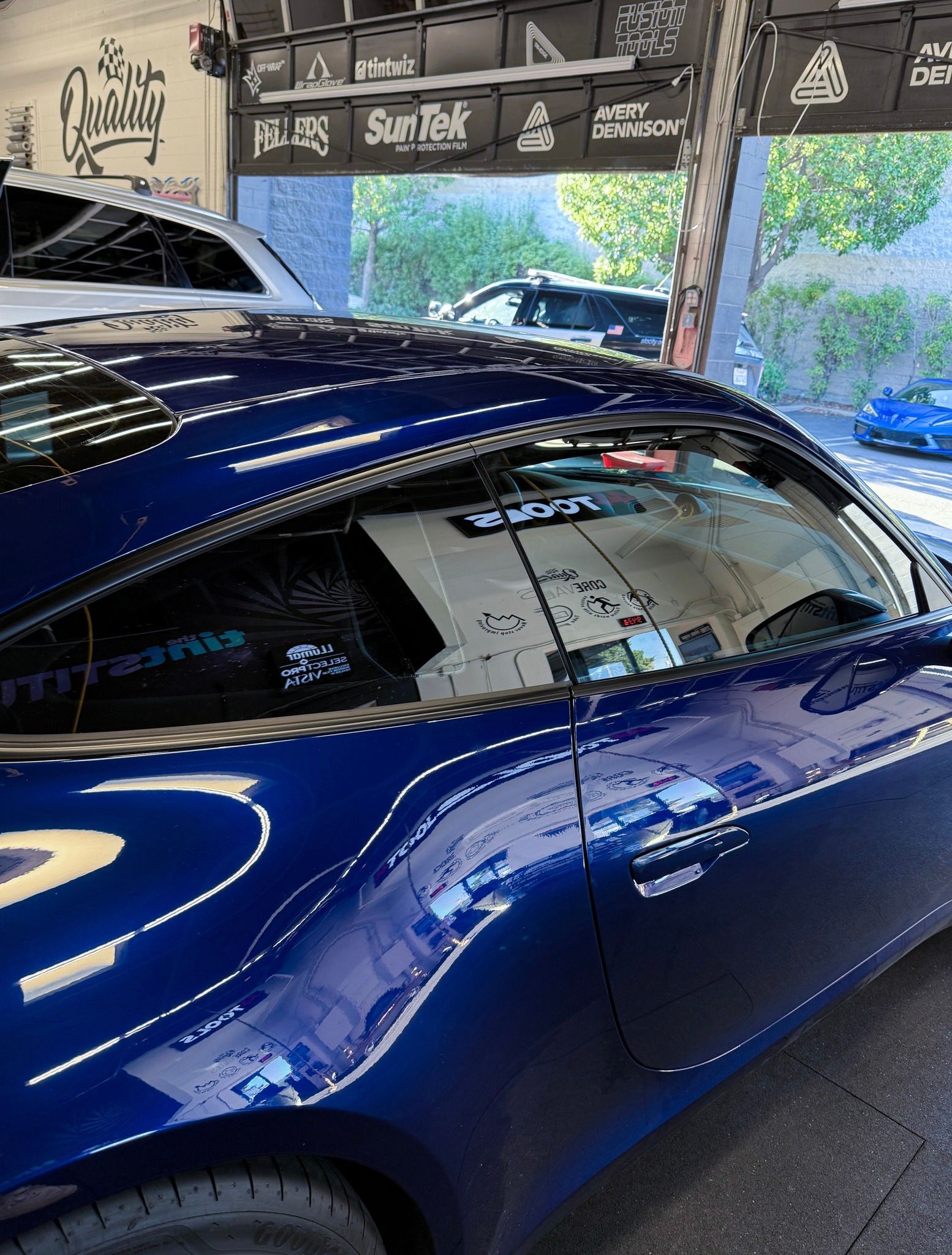 Blue sports car parked in a garage with large windows and greenery outside
