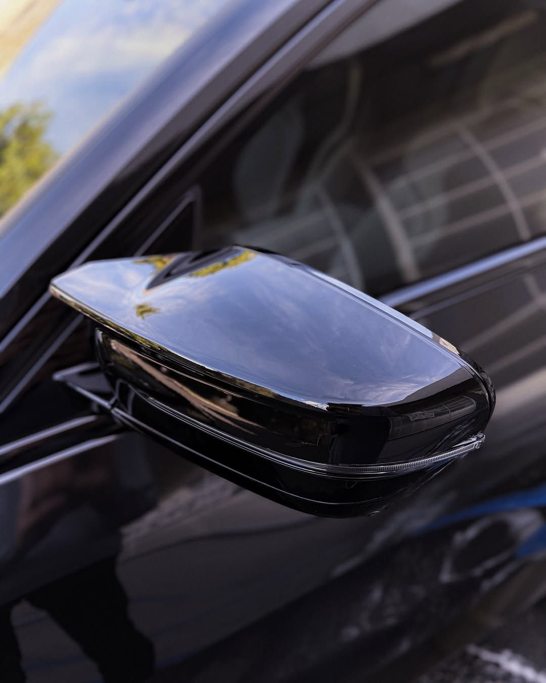 Glossy black side mirror on a dark car, reflecting the sky and nearby building