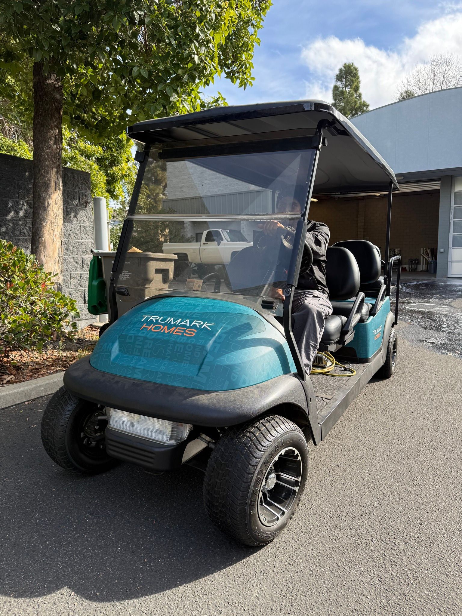 Teal golf cart parked outdoors on a sunny street, with a clear windshield and black roof.