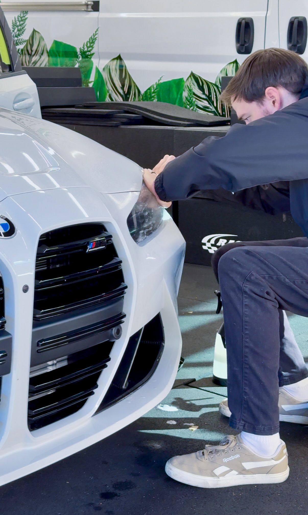 Man polishing the headlight of a white BMW in a showroom with green plants in the background