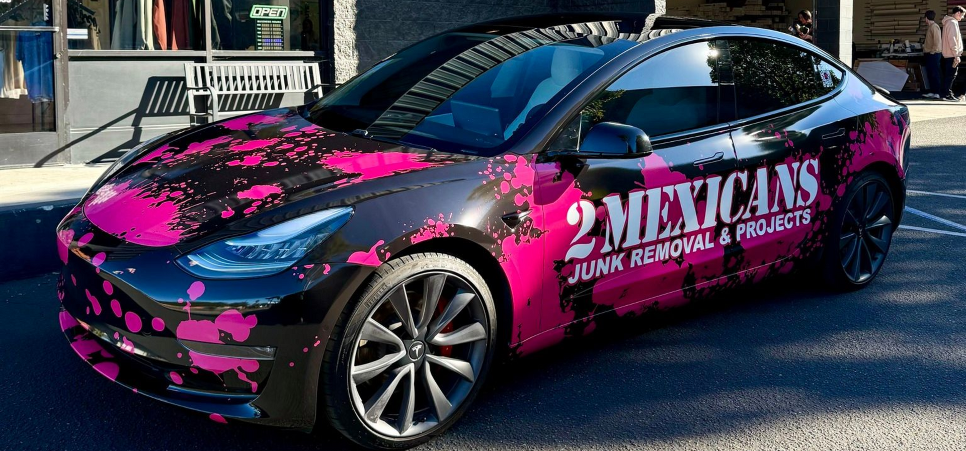 Pink-and-black wrapped race car with “MEXICARS” branding parked on a street