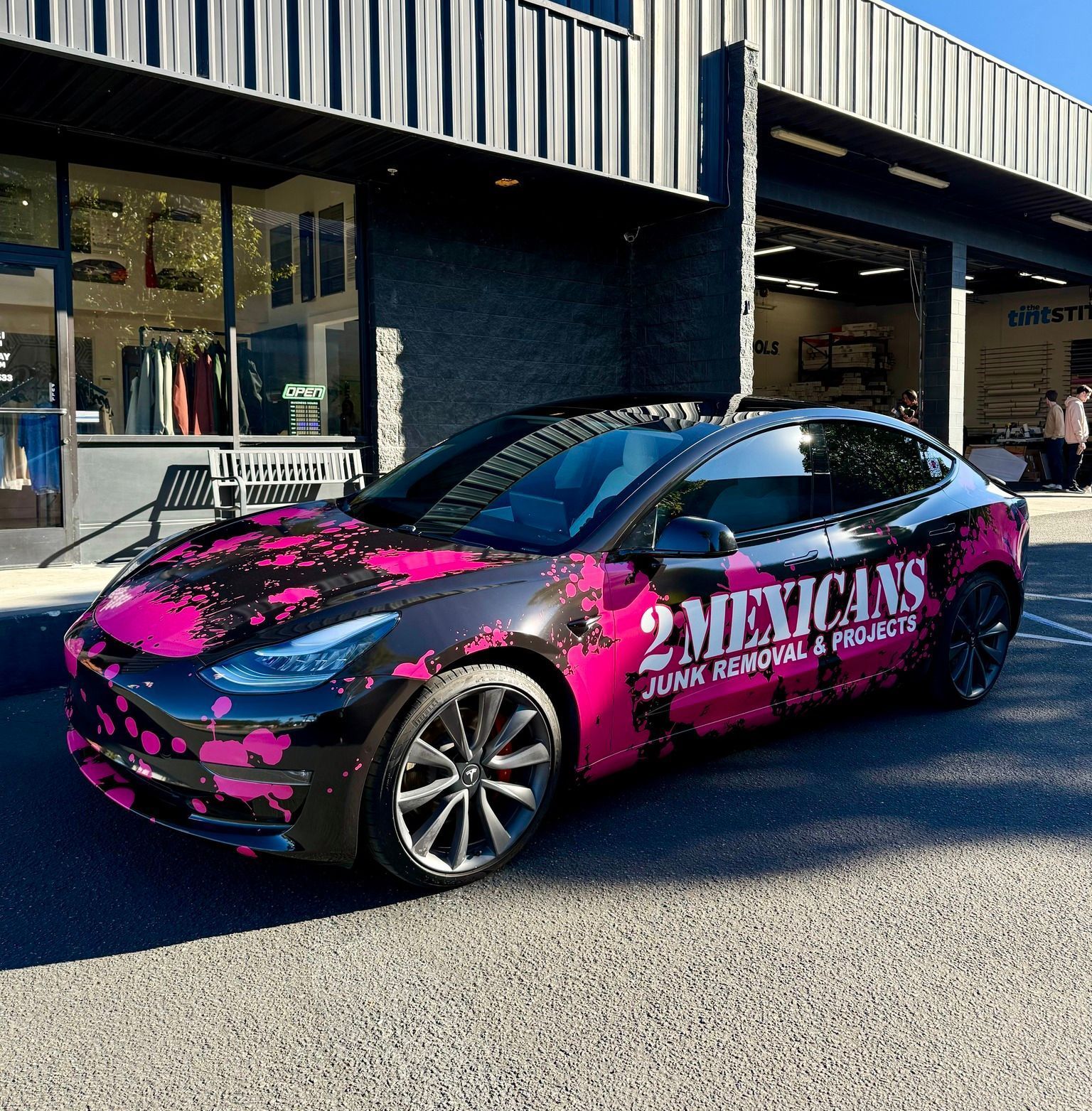 Black car with pink graphics and “2 Mexicans” text parked outside a storefront