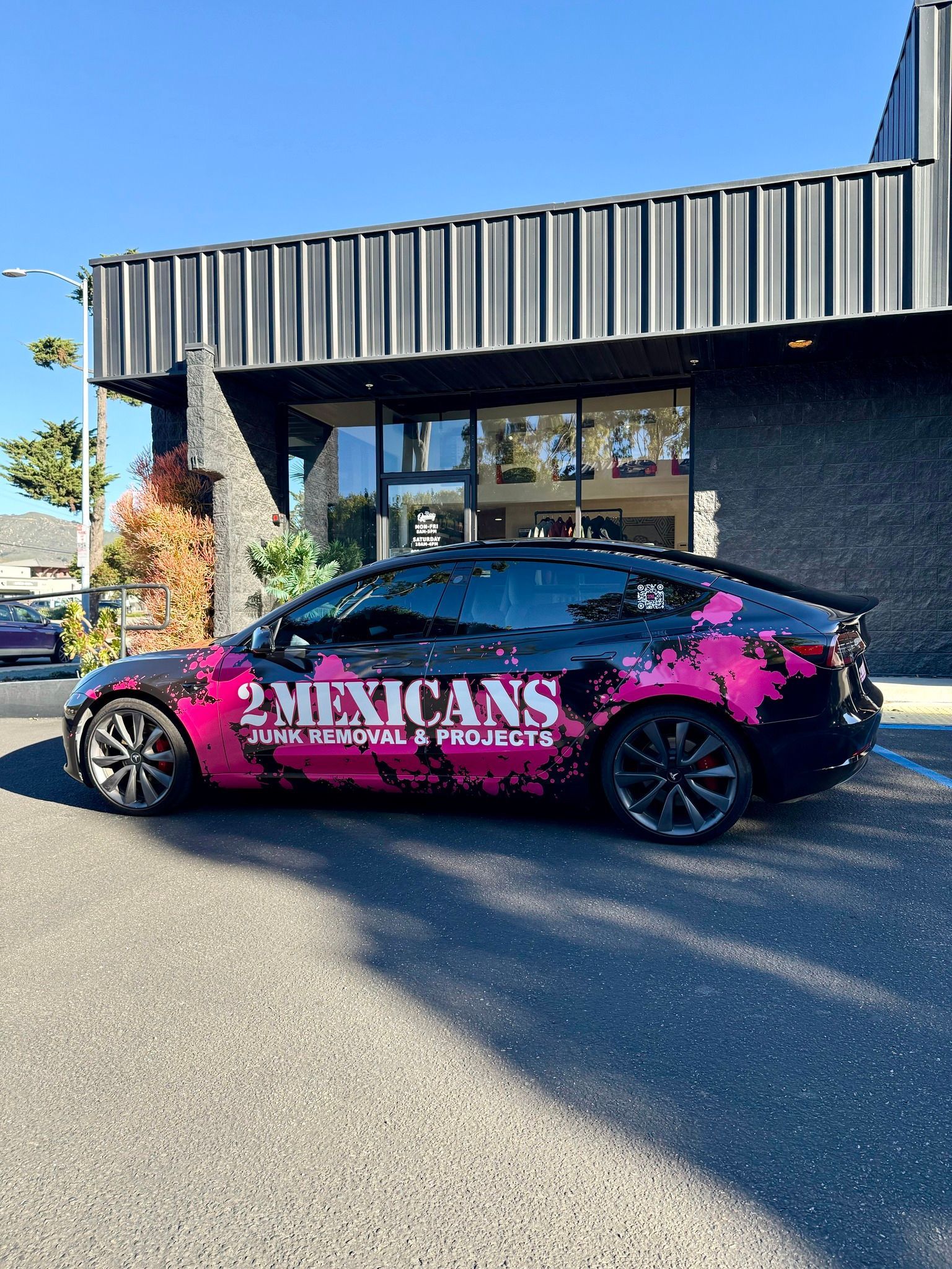 Pink-and-black wrapped car parked outside a building with “2 Mexicans” branding on the side