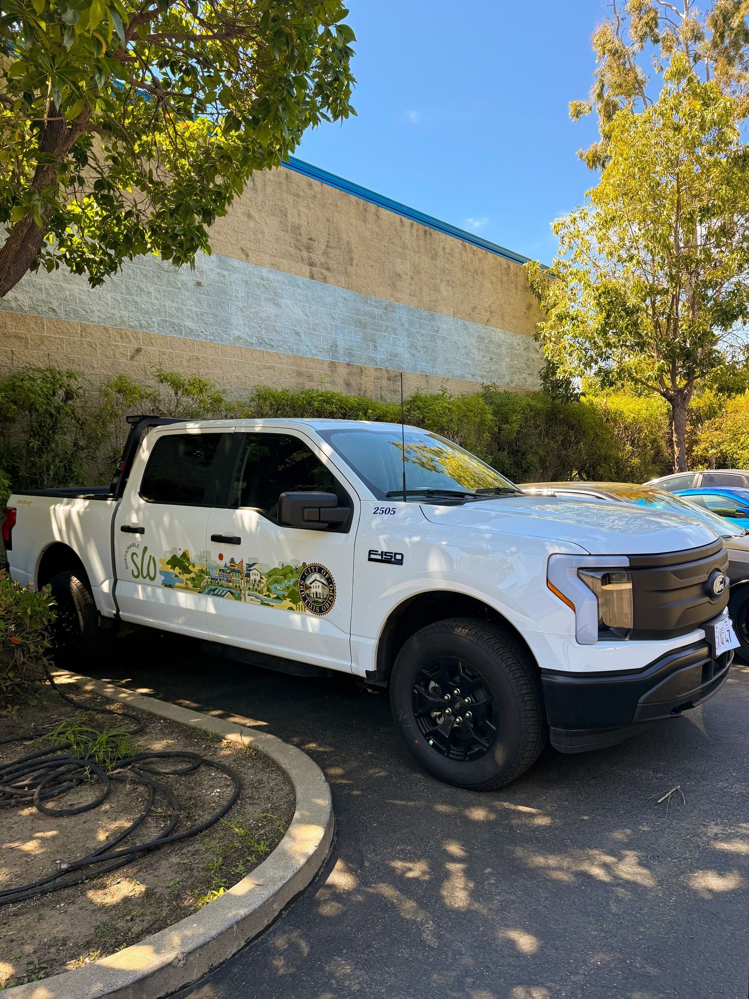 White pickup truck parked beside a building under trees on a sunny day