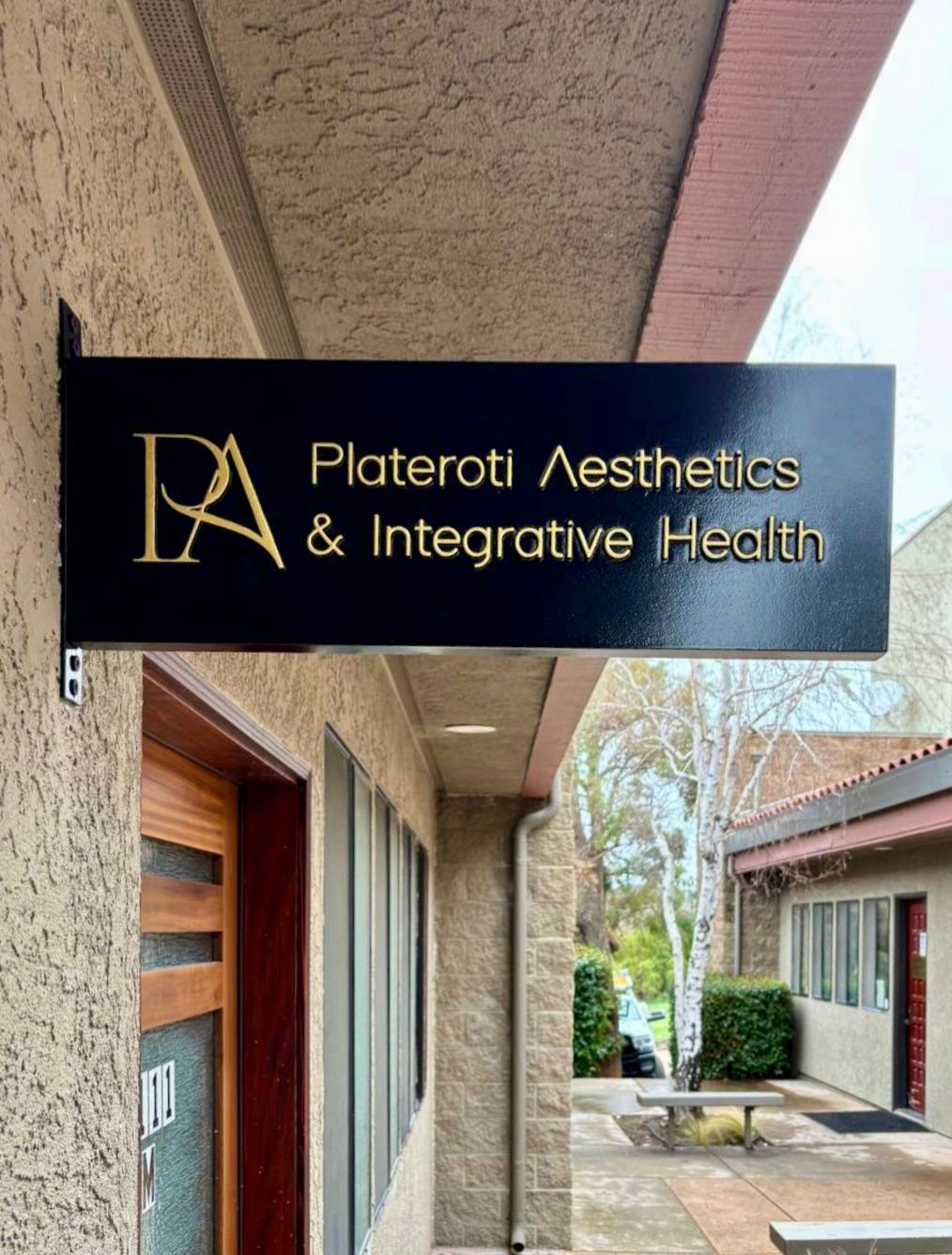 Black sign for “Plateroti Aesthetics & Integrative Health” outside a building entrance