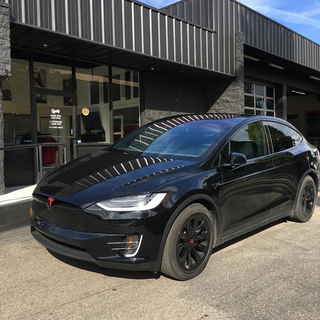 Black Tesla SUV parked outside a modern building in sunlight