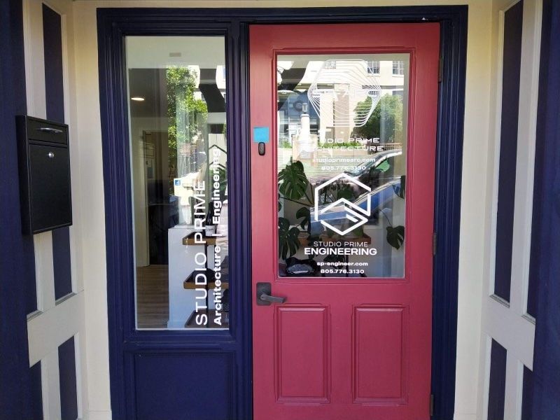 Pink storefront door with glass panels and a black mailbox on a blue-and-cream exterior wall