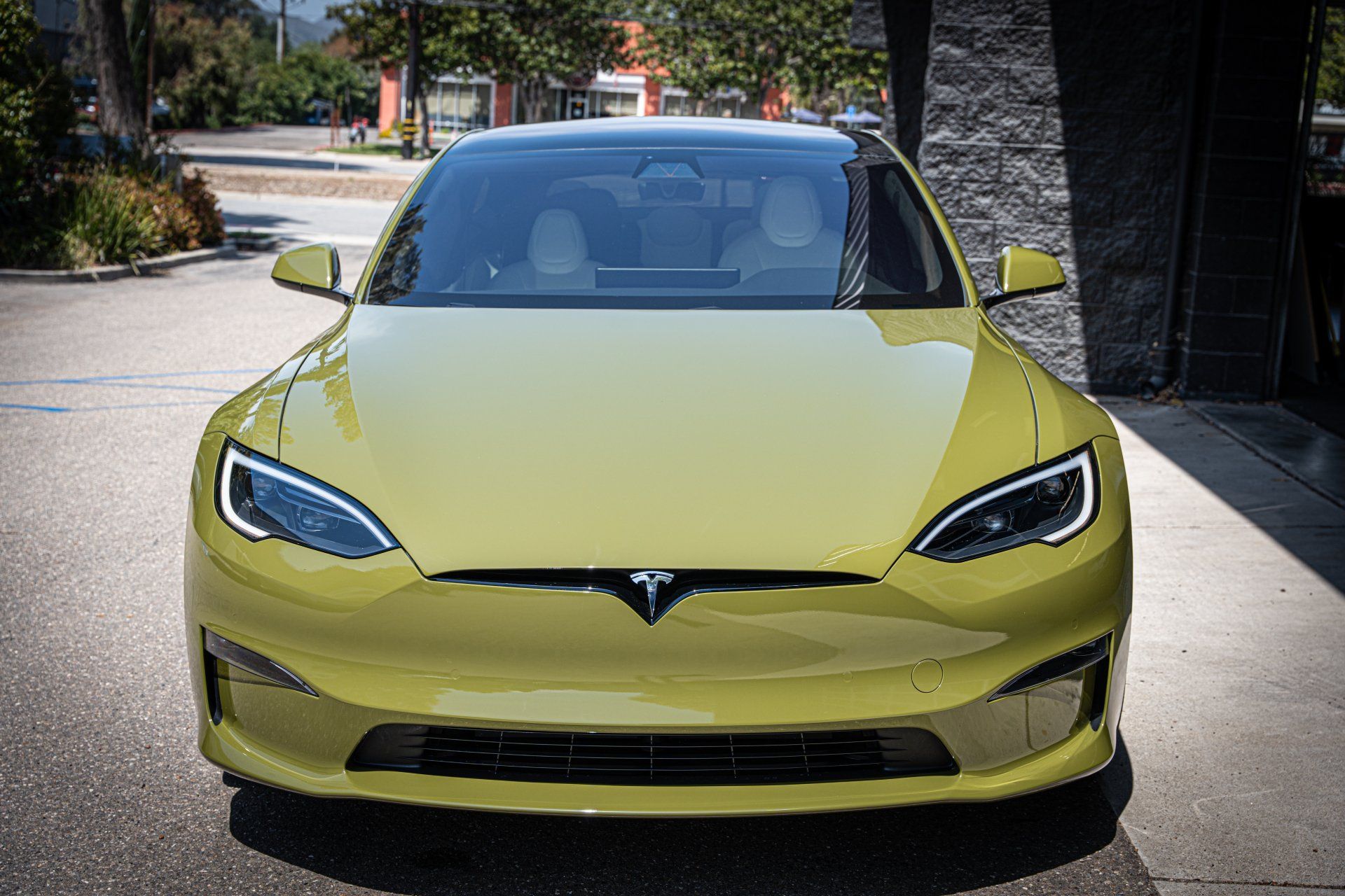 Yellow Tesla Model S parked outdoors in a driveway, front view.