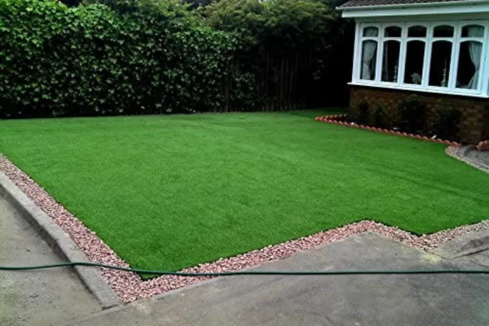 Freshly laid green lawn bordered by pink gravel, beside a house with bay windows and hedges