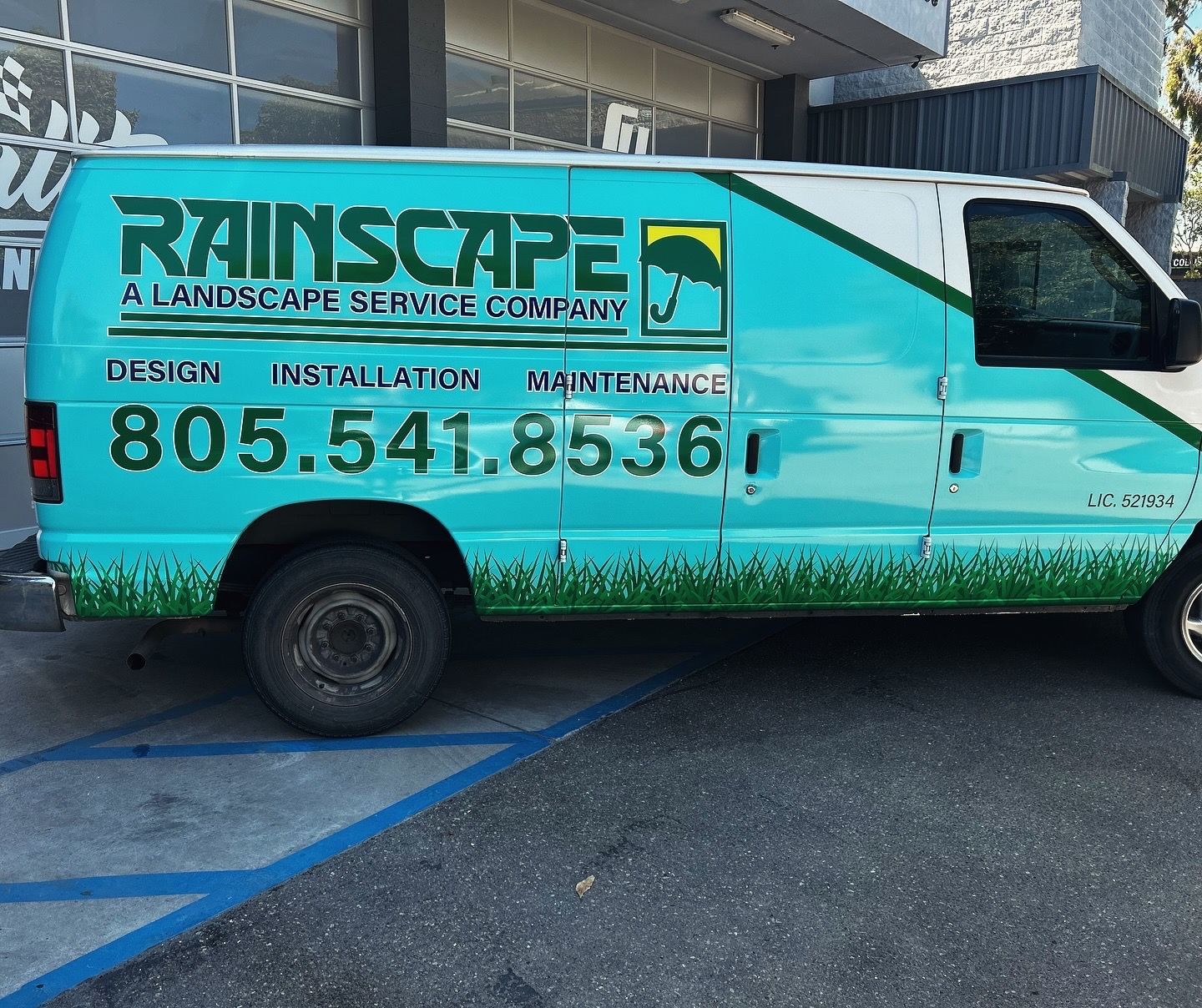 Turquoise RainScape landscaping service van parked in a lot, with website and phone number on the side