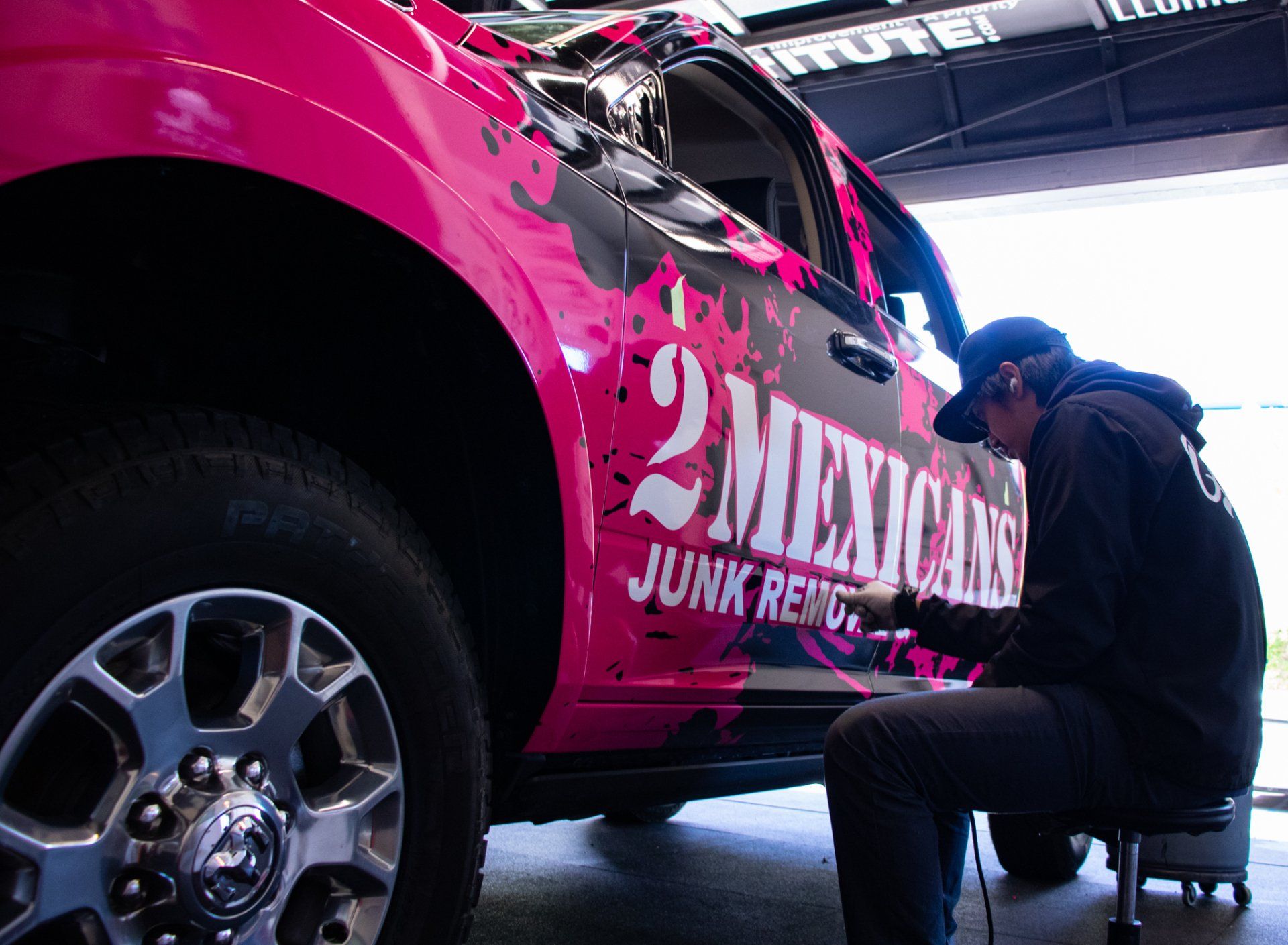 Mechanic kneeling beside a pink race car, working near the front wheel in a garage.