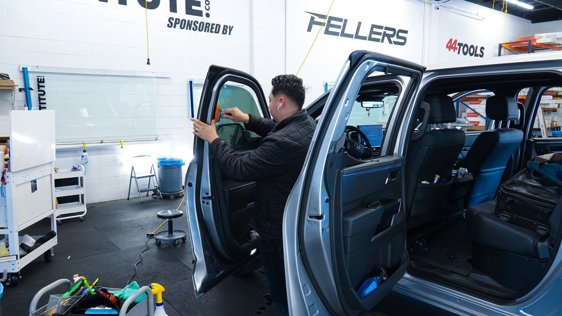 Technician leaning into a blue car in a garage, working on the open front door.