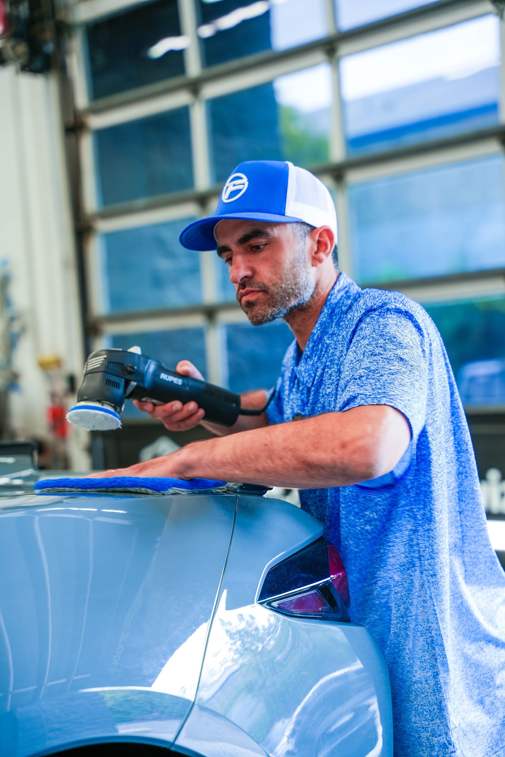 Mechanic polishing a blue car with a buffer in an auto shop