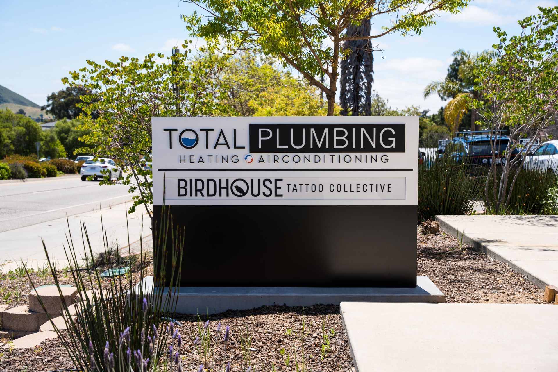 Business sign for Total Plumbing and Birdhouse Patio Collective in a sunny outdoor plaza