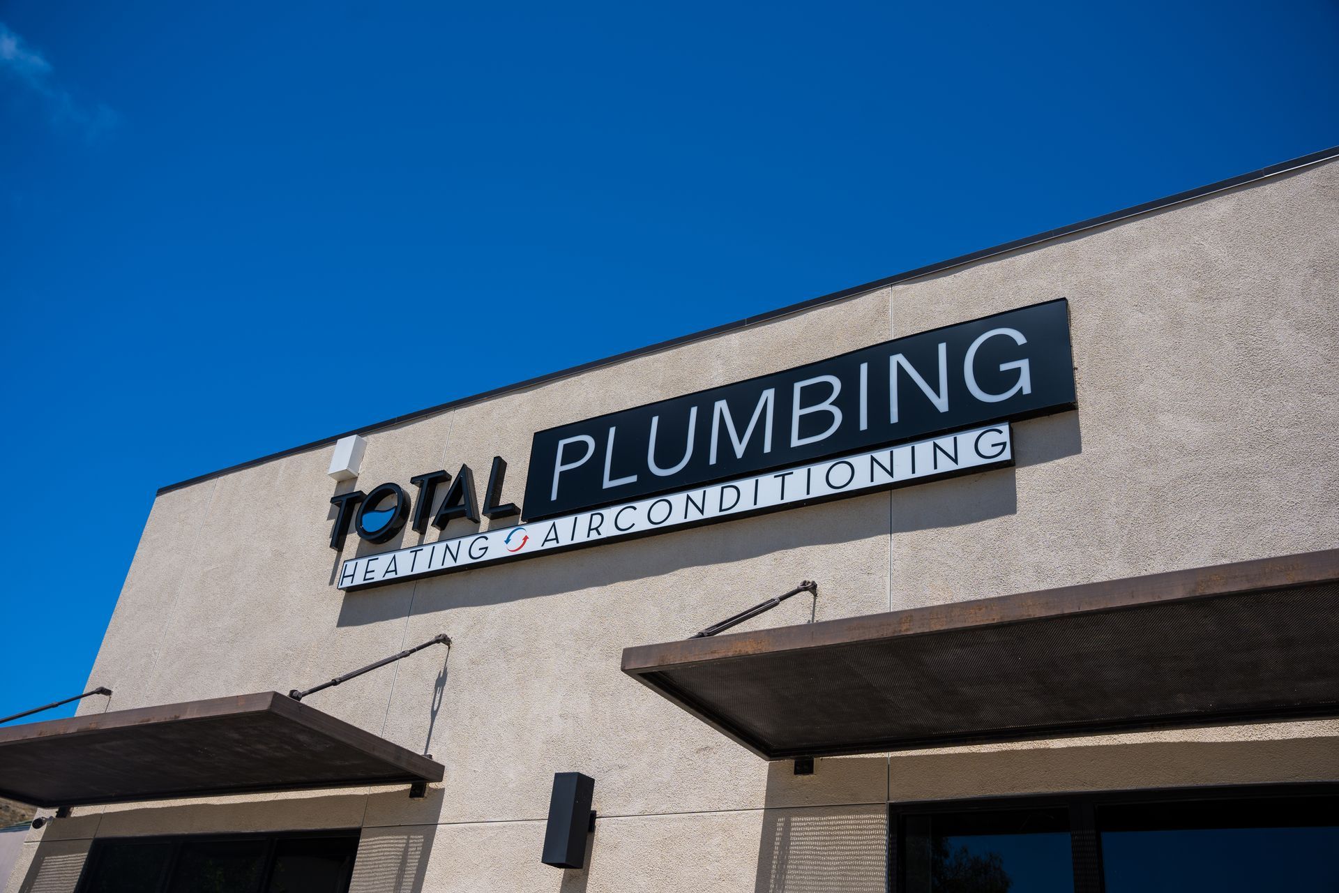 OTM Plumbing storefront sign on a beige building under a clear blue sky