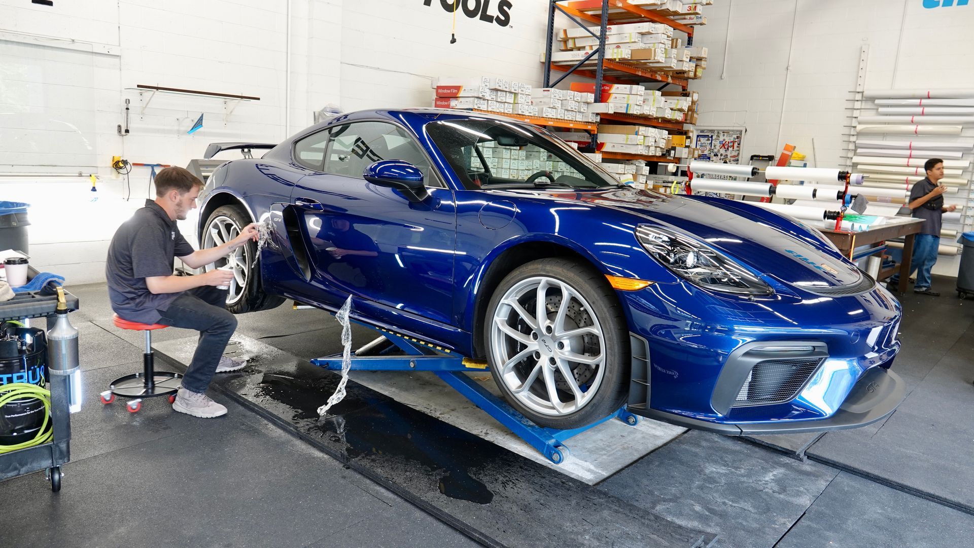 Blue sports car on a lift in a workshop, with a mechanic working on the front wheel.