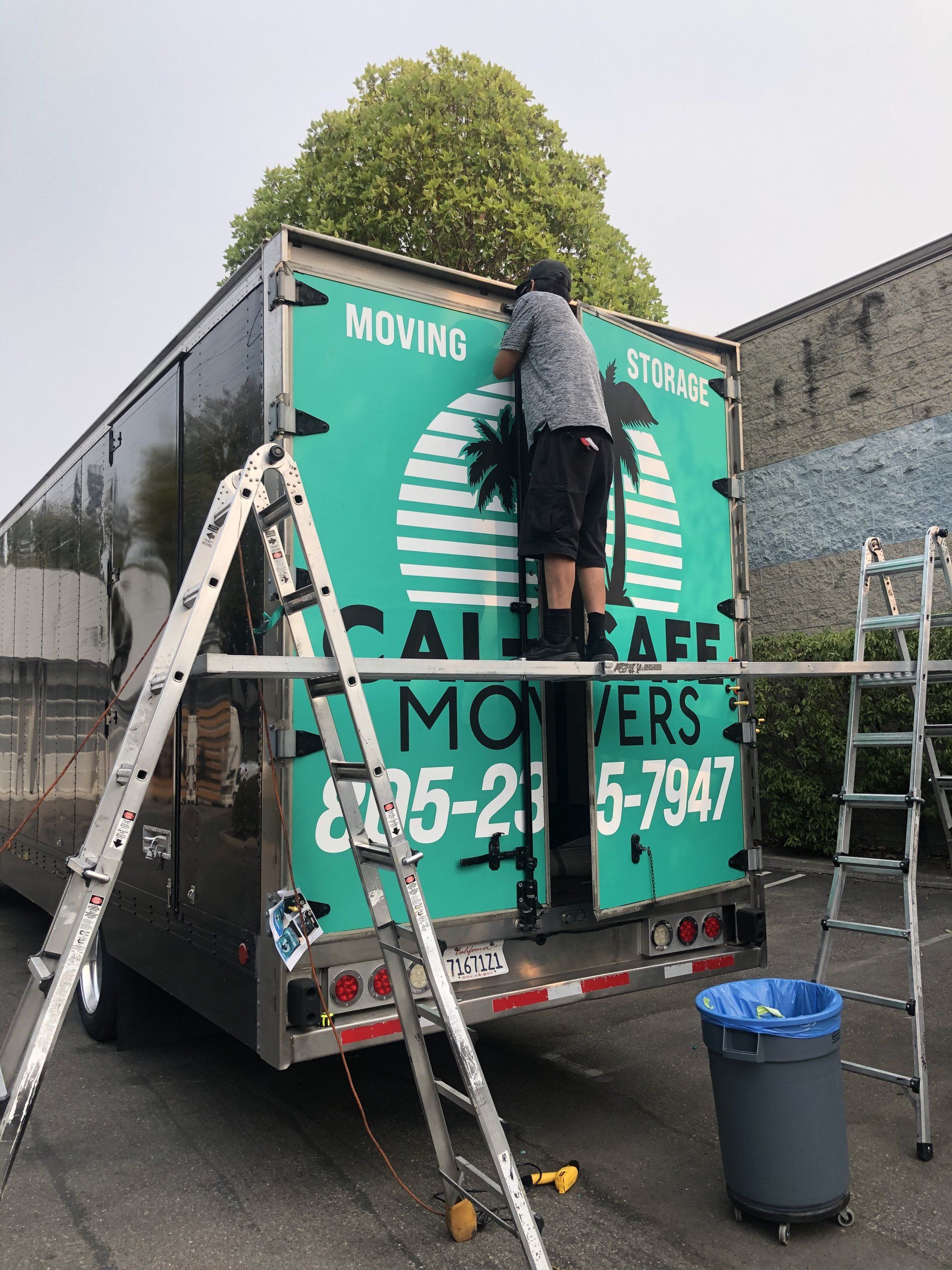 Person on ladder cleaning the back of a green moving truck outdoors