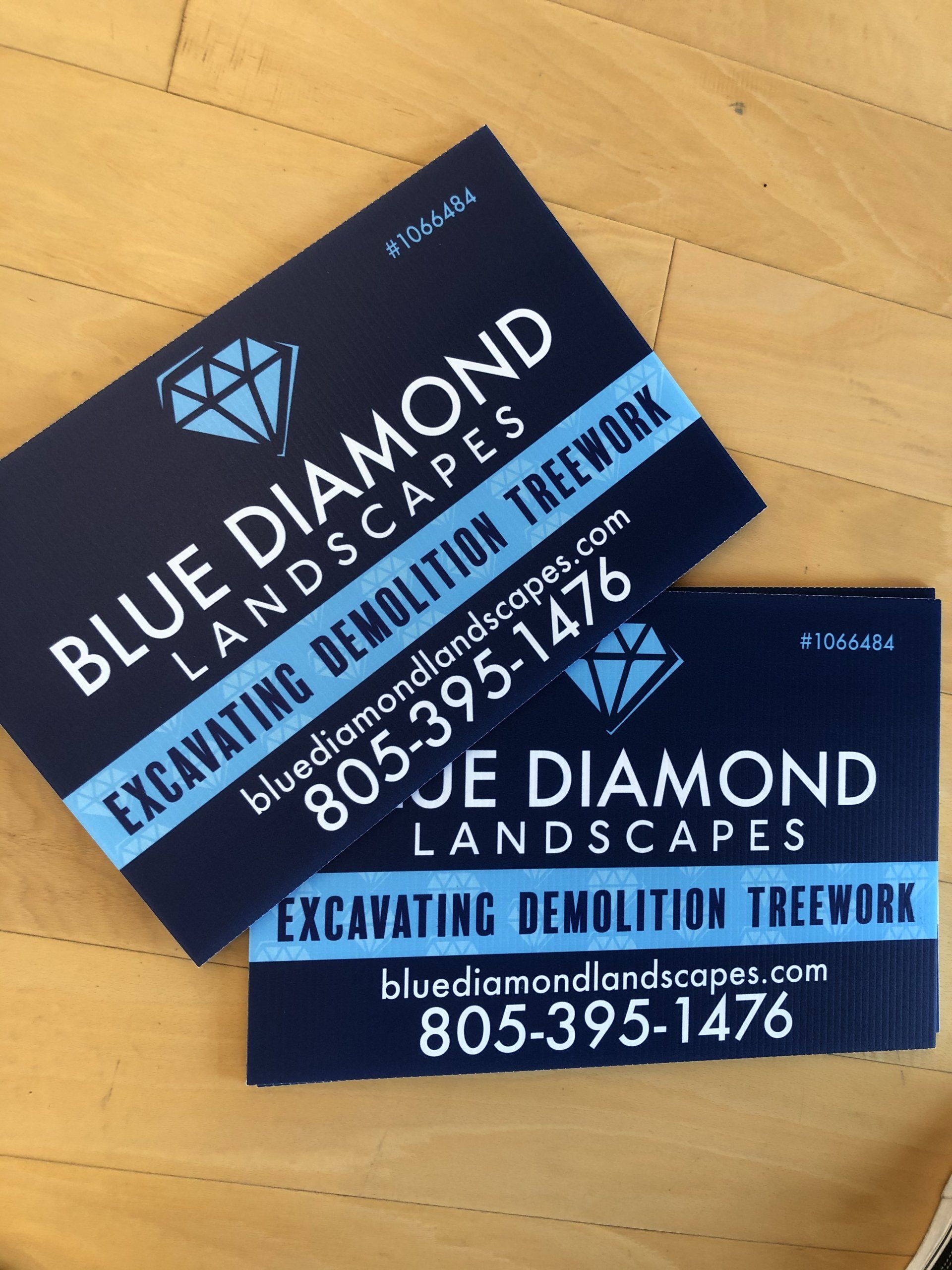 Blue Diamond Landscapes business cards stacked on a wooden surface, navy and light blue design.
