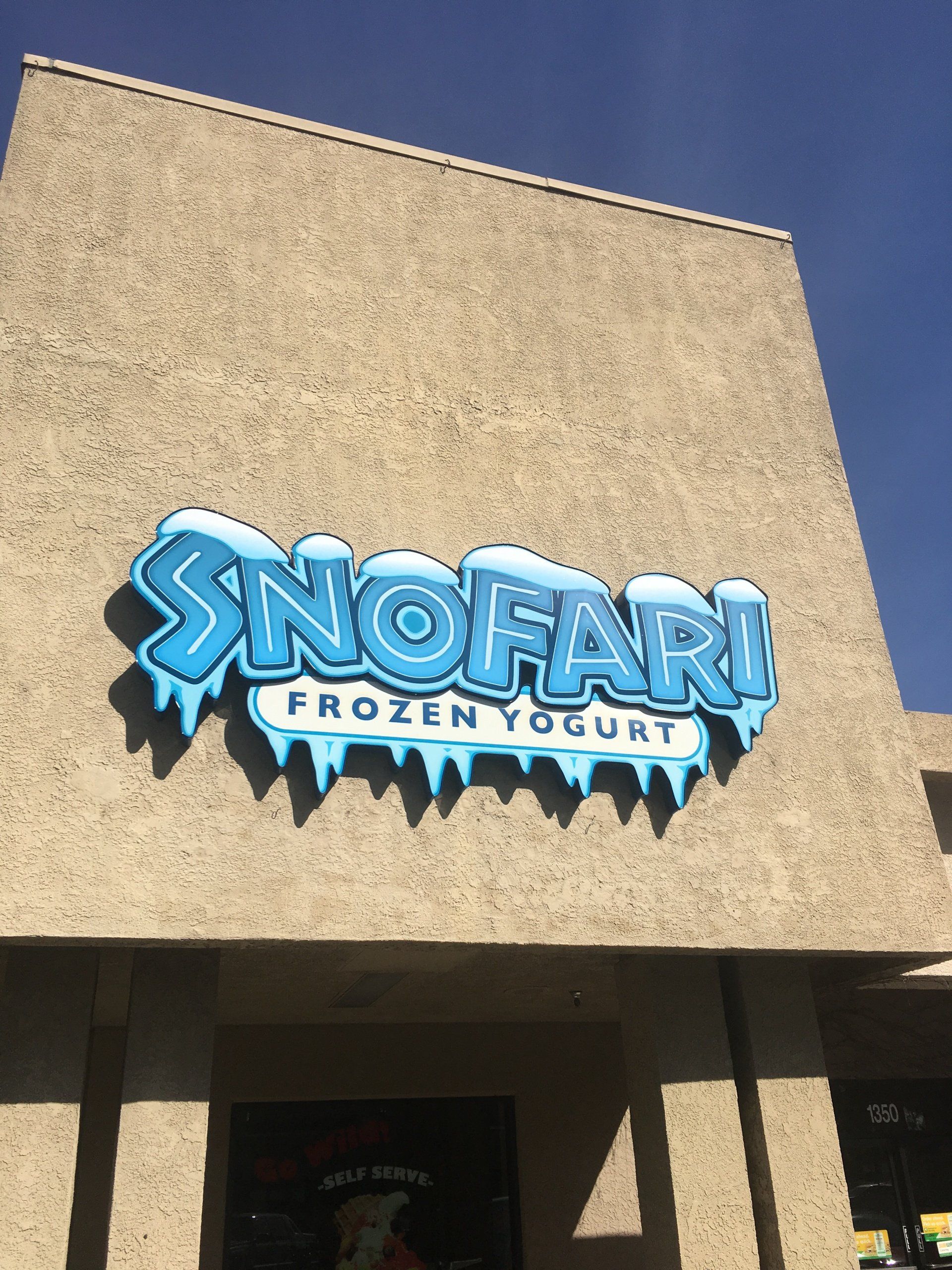 Snofari Frozen Yogurt sign on a beige storefront under a blue sky