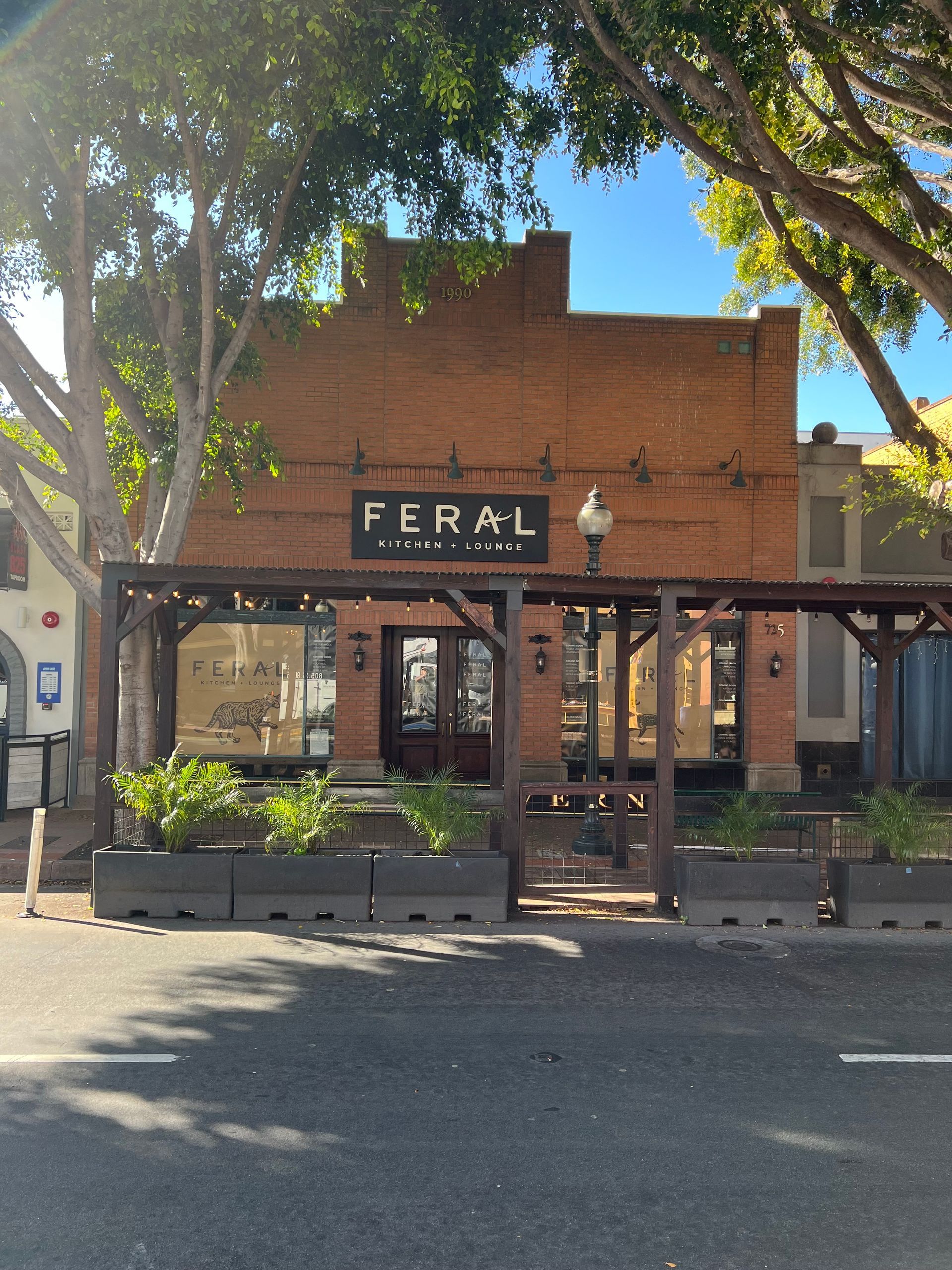 Brick storefront with a FERAL sign, shaded patio, and trees lining the street
