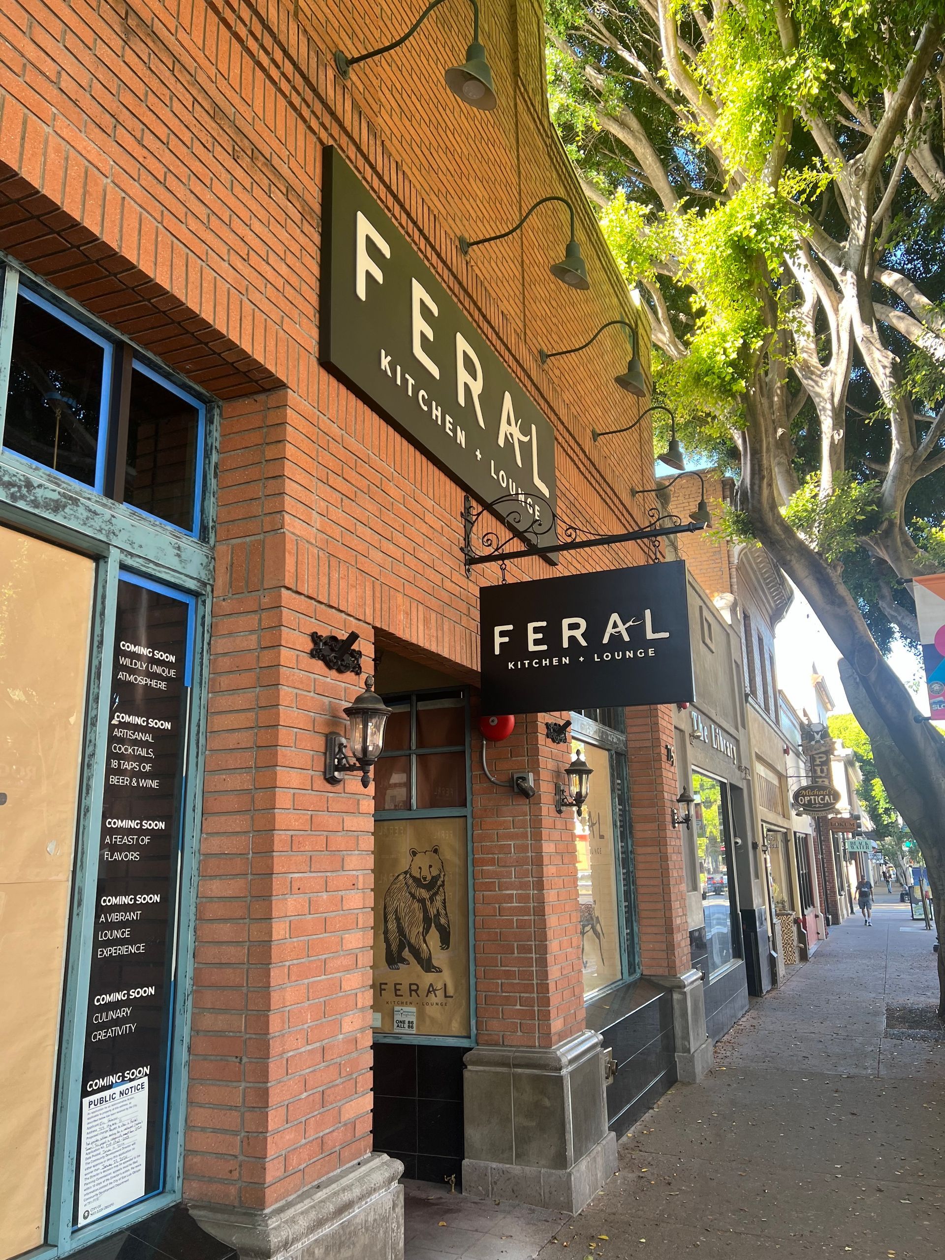 Brick storefront with FERAL signage and awning along a tree-lined sidewalk