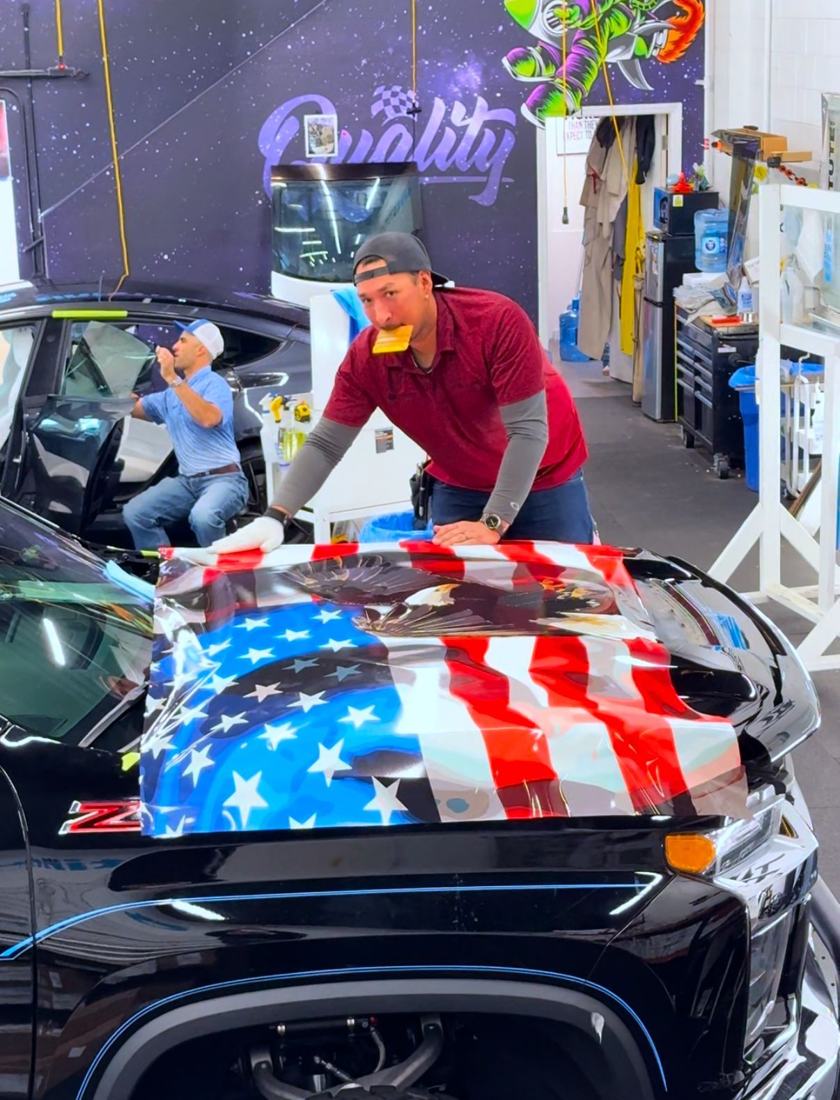 Man polishing a black car hood with an American flag design in an auto detailing shop