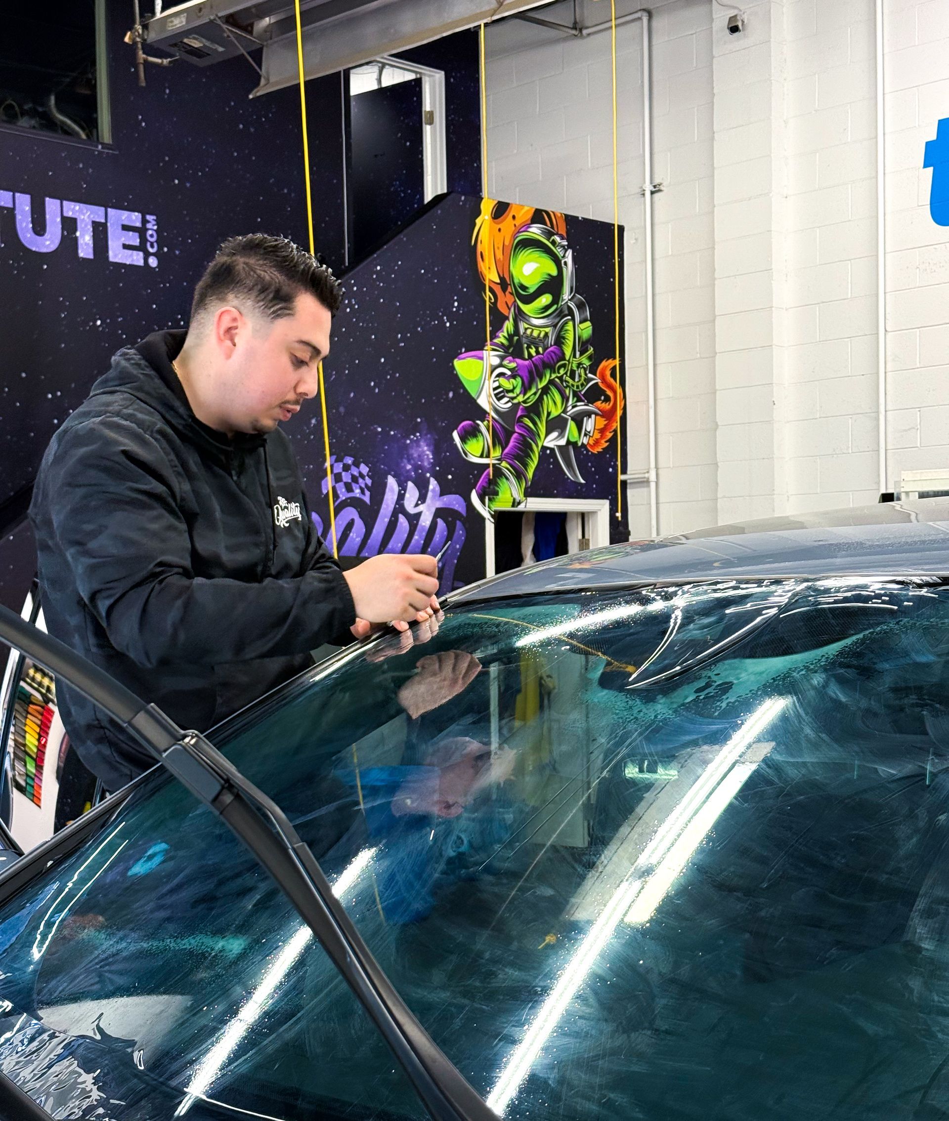 Man using a tool to work on a car windshield in an auto shop