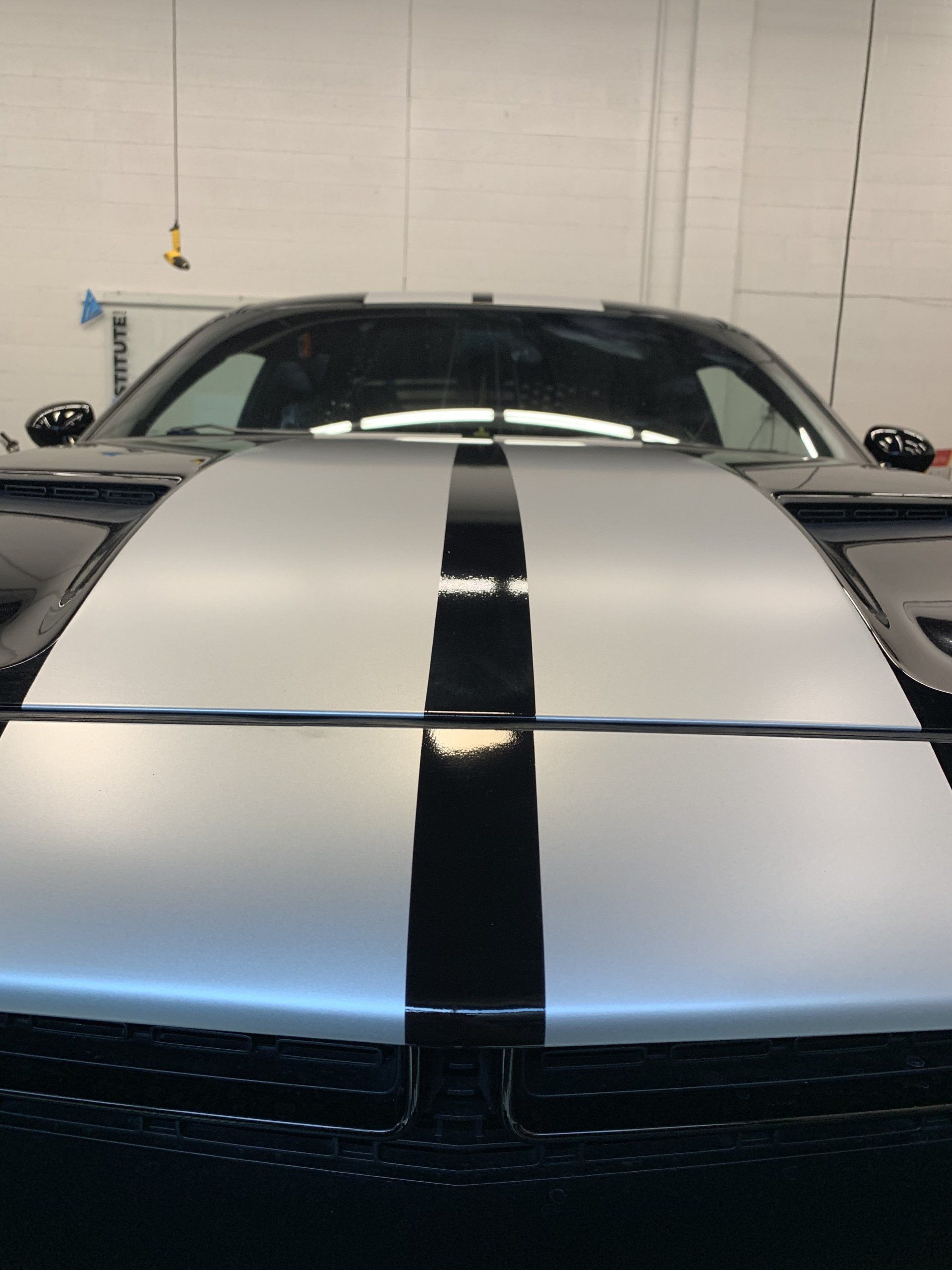 Front view of a silver sports car with black racing stripes in a garage.