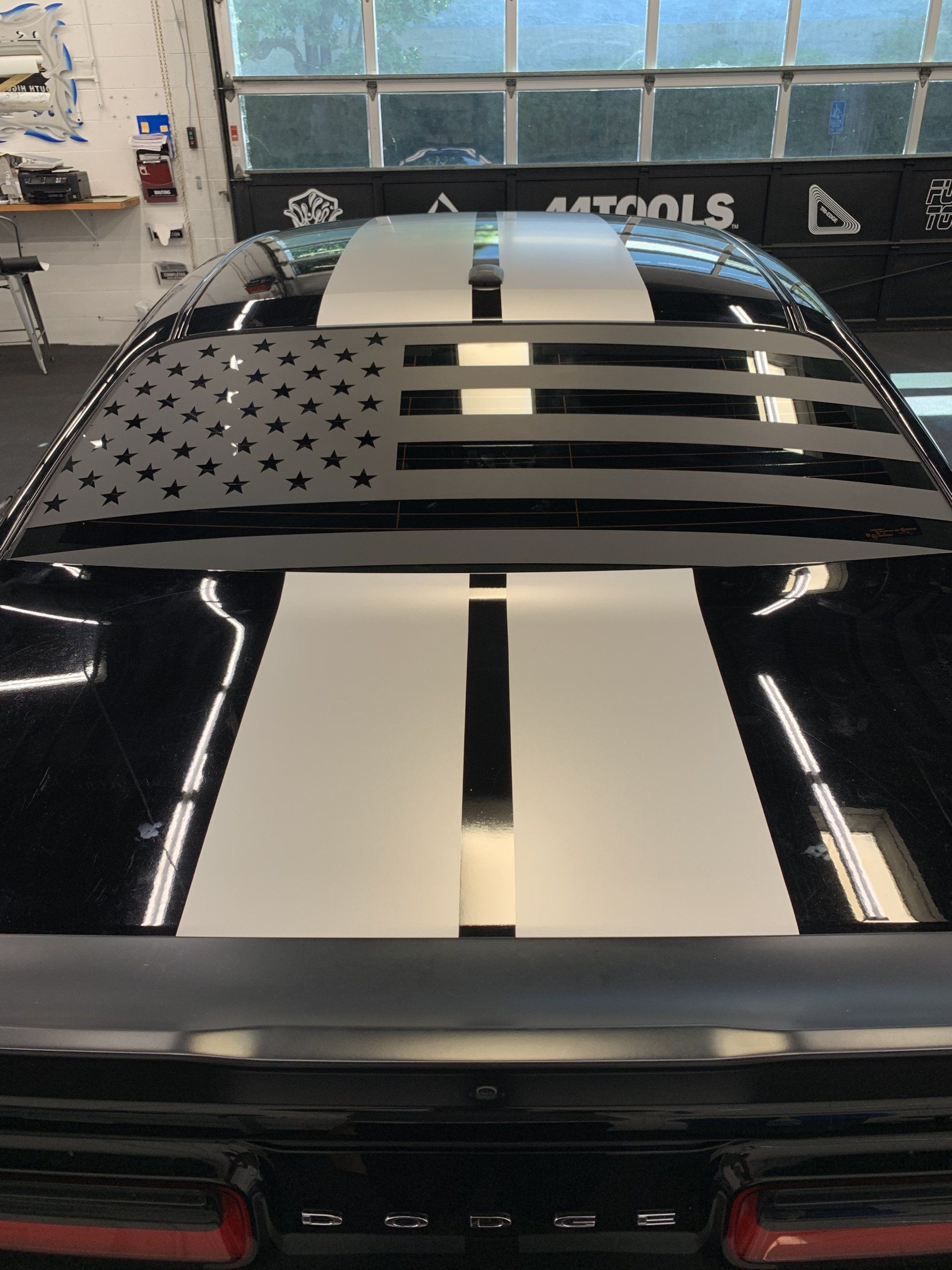 Black sports car in a garage with a glossy hood and an American flag roof graphic.