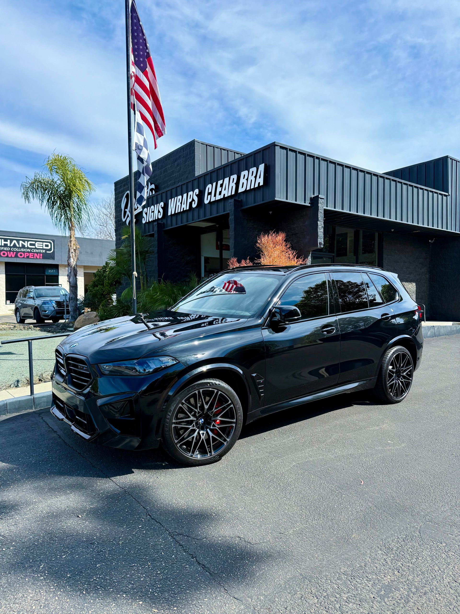 Black SUV parked outside a car dealership with an American flag flying nearby.