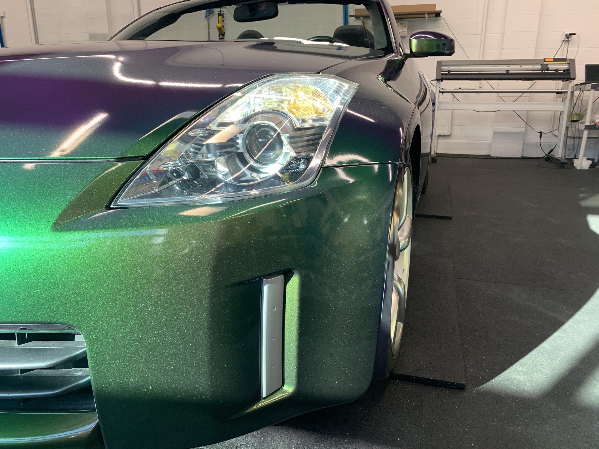 Close-up of a green sports car’s front corner in a garage, showing the headlight and bumper.