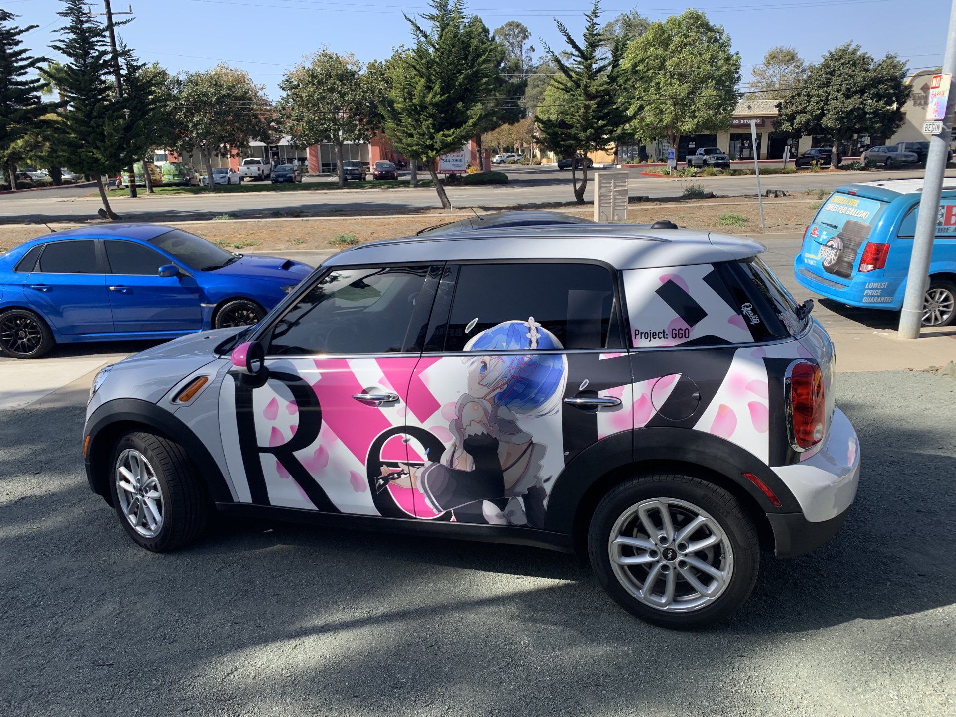 Compact car with pink-and-black wrap parked on a street, with blue cars and trees in the background